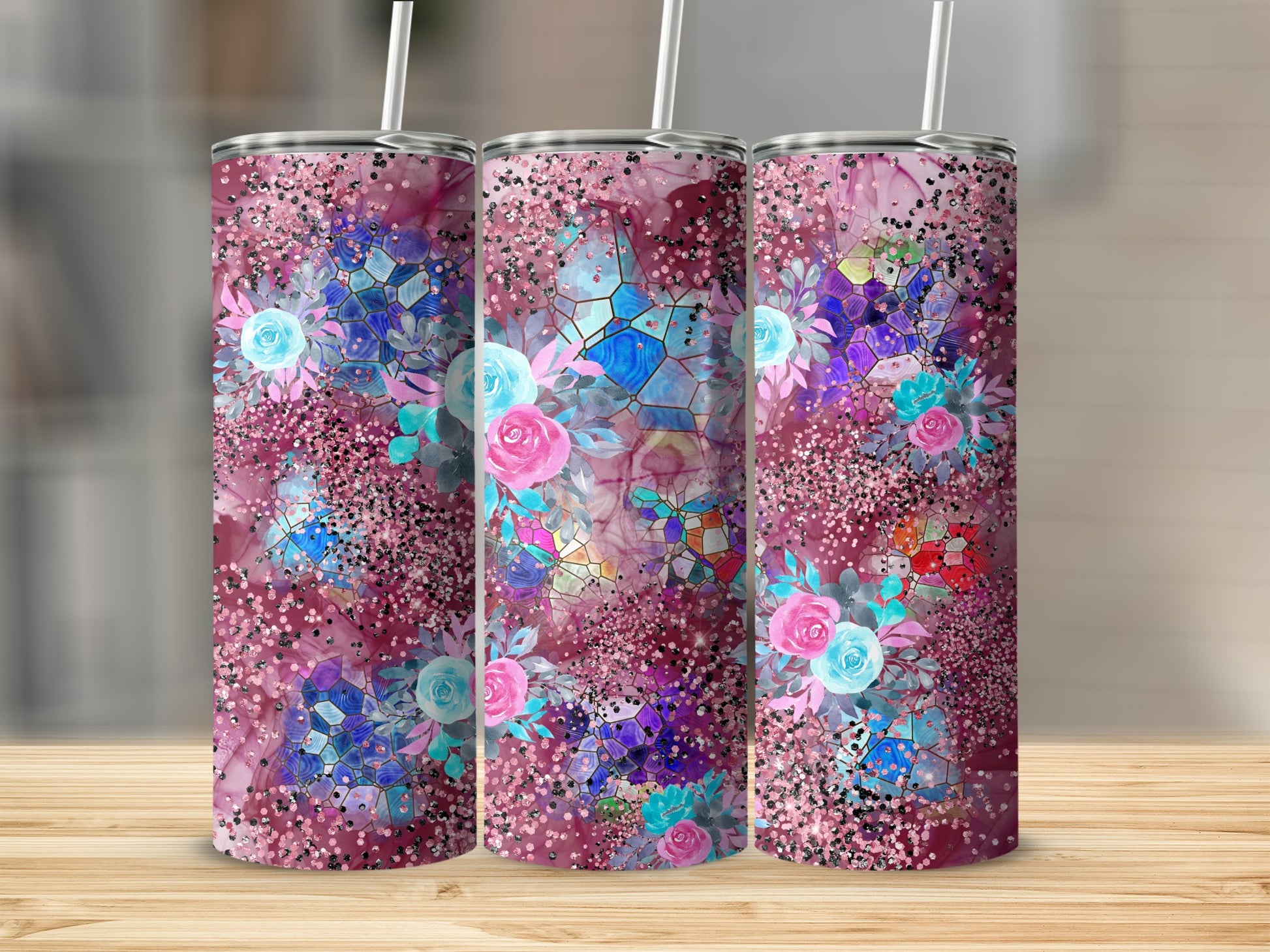 Three tall tumblers with floral and glitter designs on a wooden surface.