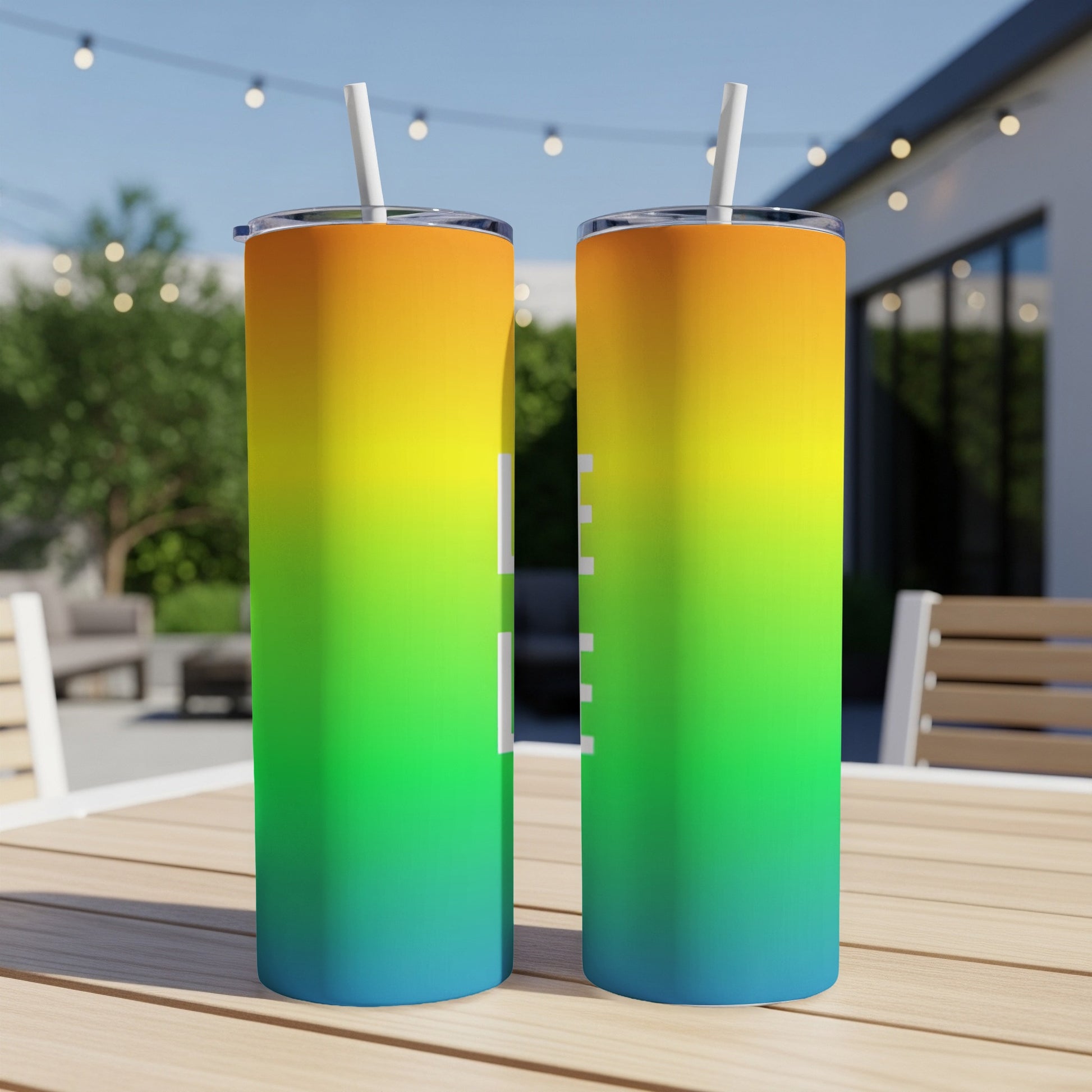 Two tumblers with a rainbow gradient design, sitting on a wooden table.