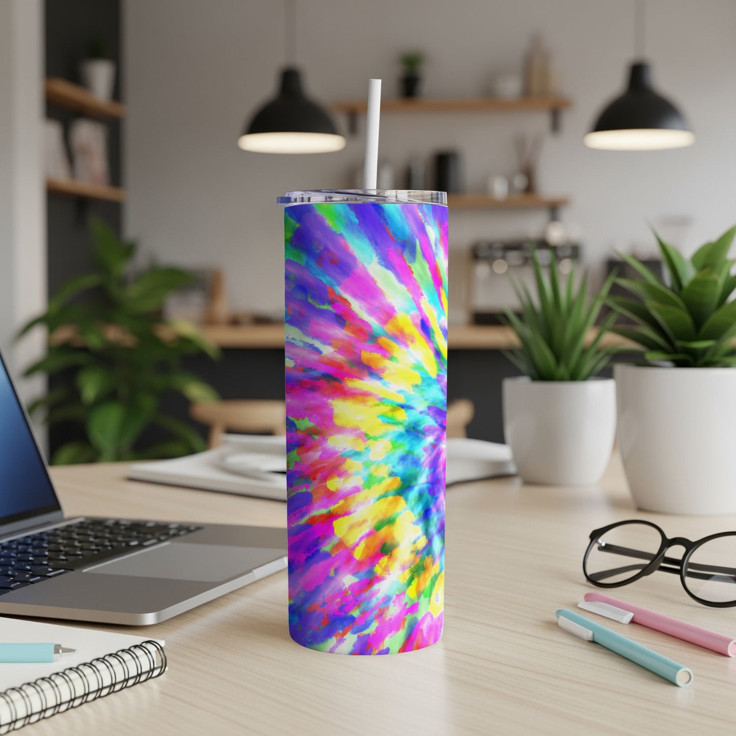 Colorful tie-dye tumbler with straw on a desk next to a laptop.