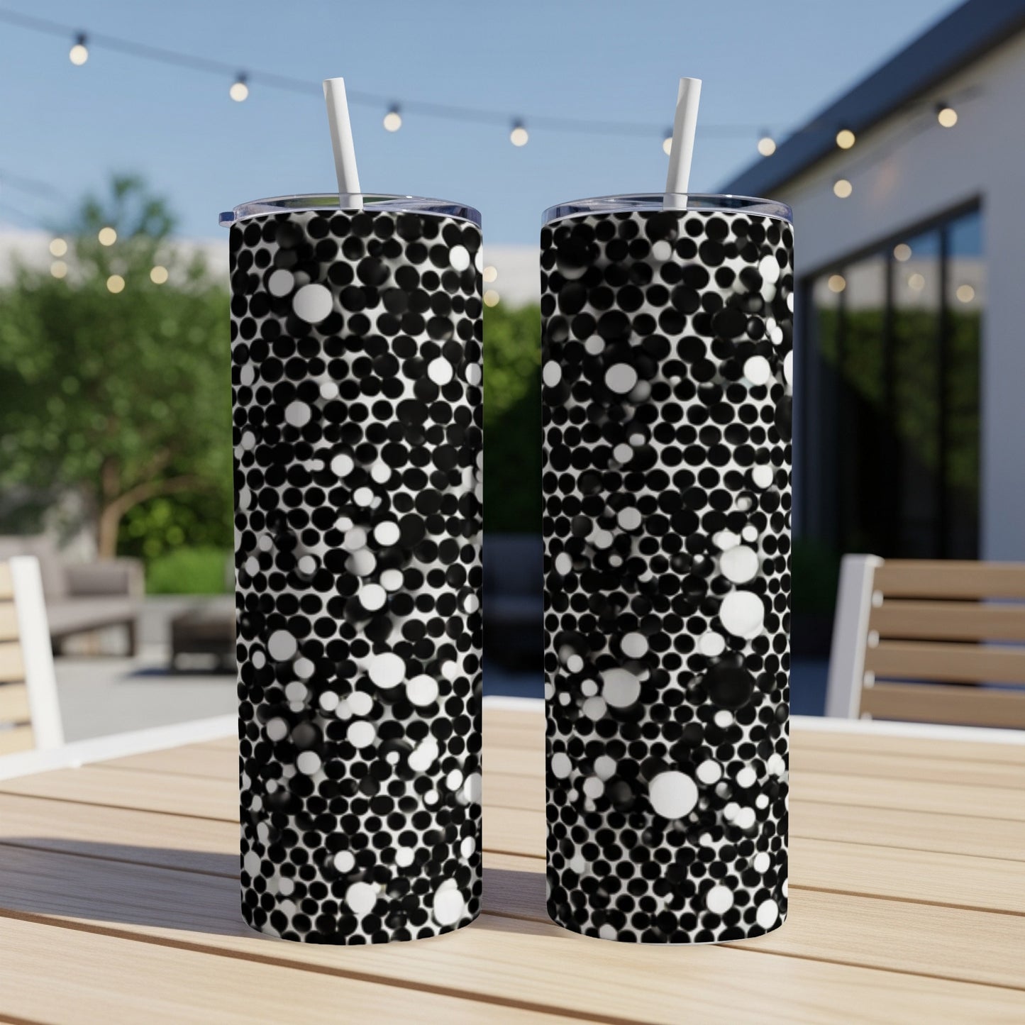 Two tumblers with a black and white bubbly dot pattern on a wooden table outdoors.