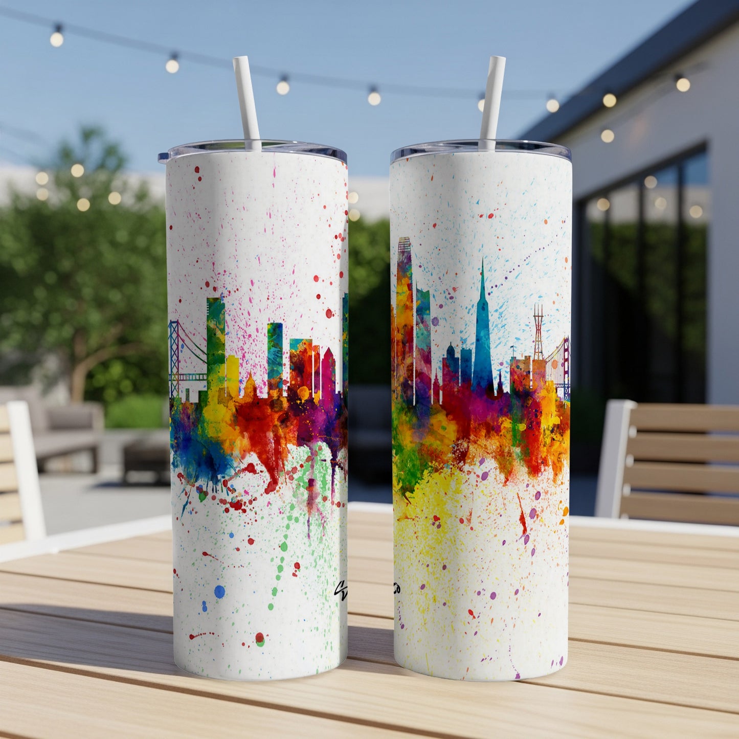 Two white tumblers with colorful watercolor city skyline designs and straws.