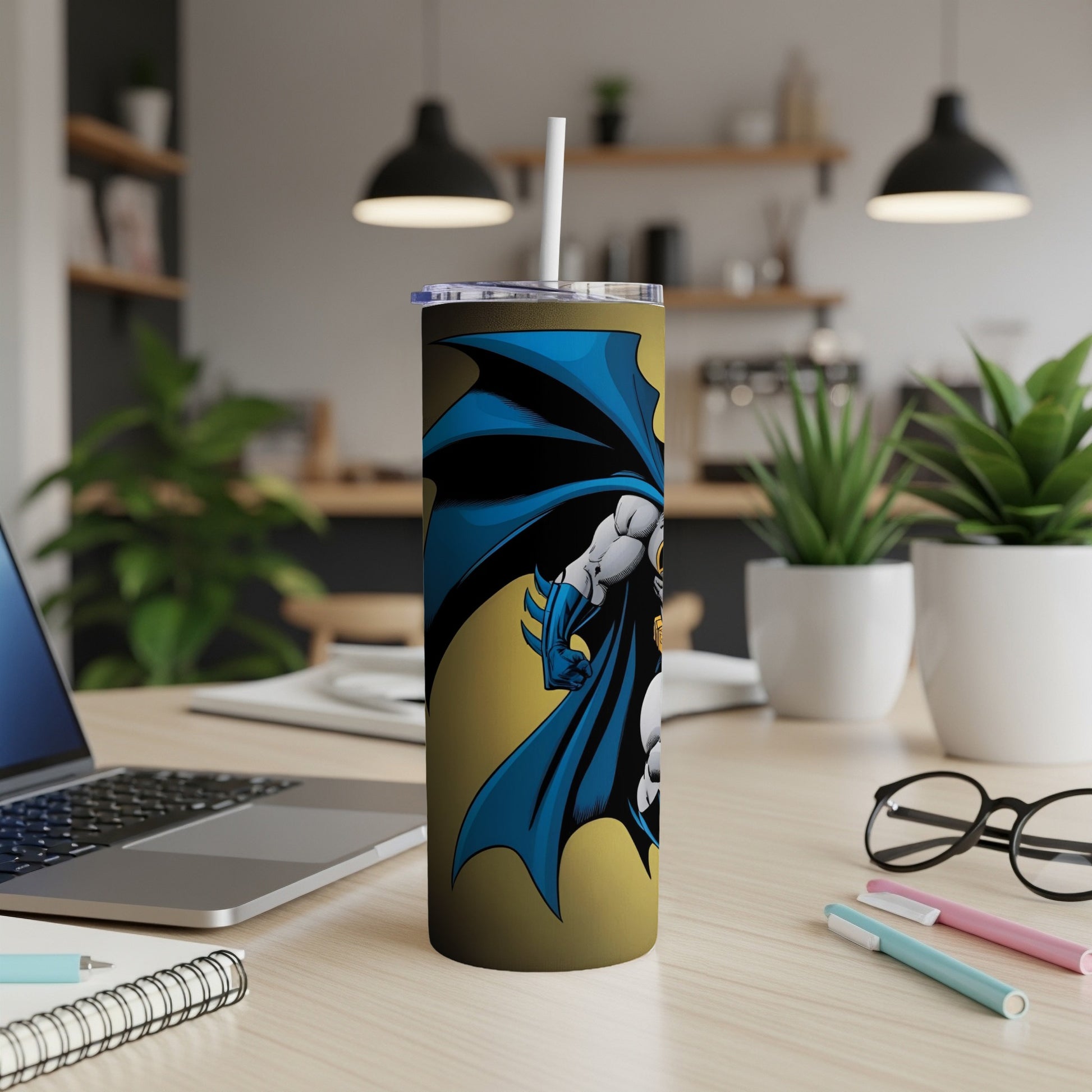 Batman tumbler with straw on a desk with a laptop and plants.