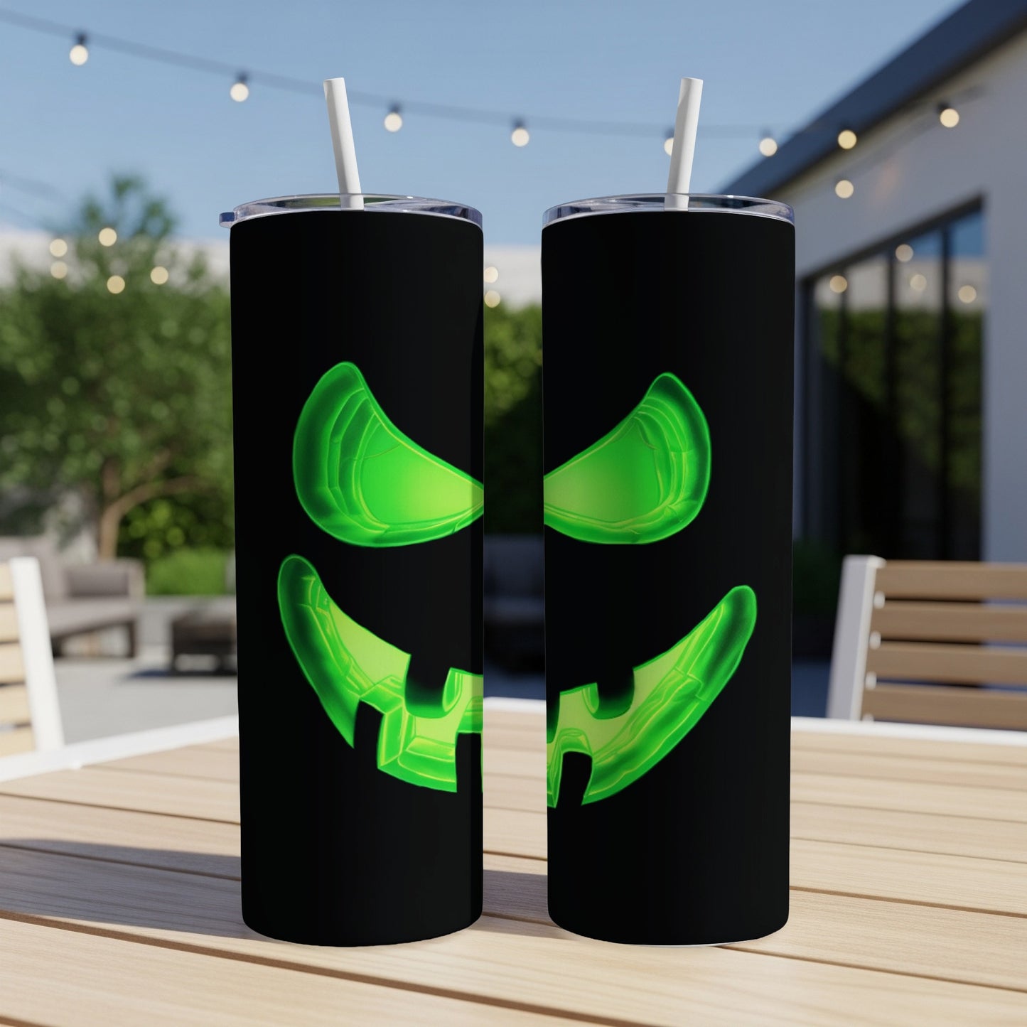 Two black tumblers with glowing green jack-o'-lantern faces, each with a straw.