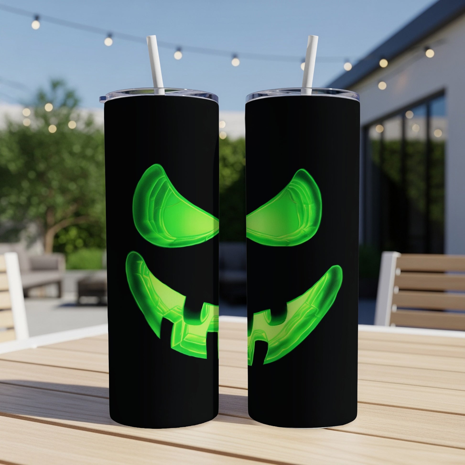 Two black tumblers with glowing green jack-o'-lantern faces, each with a straw.