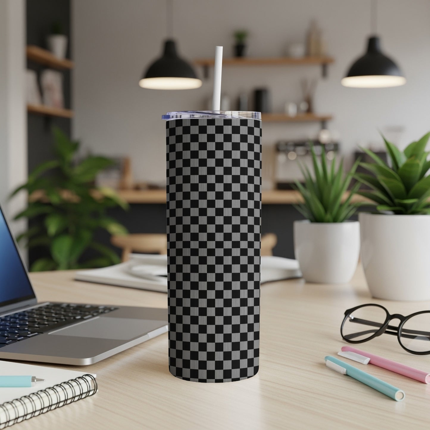 Checkerboard pattern skinny tumbler with white straw on a desk.