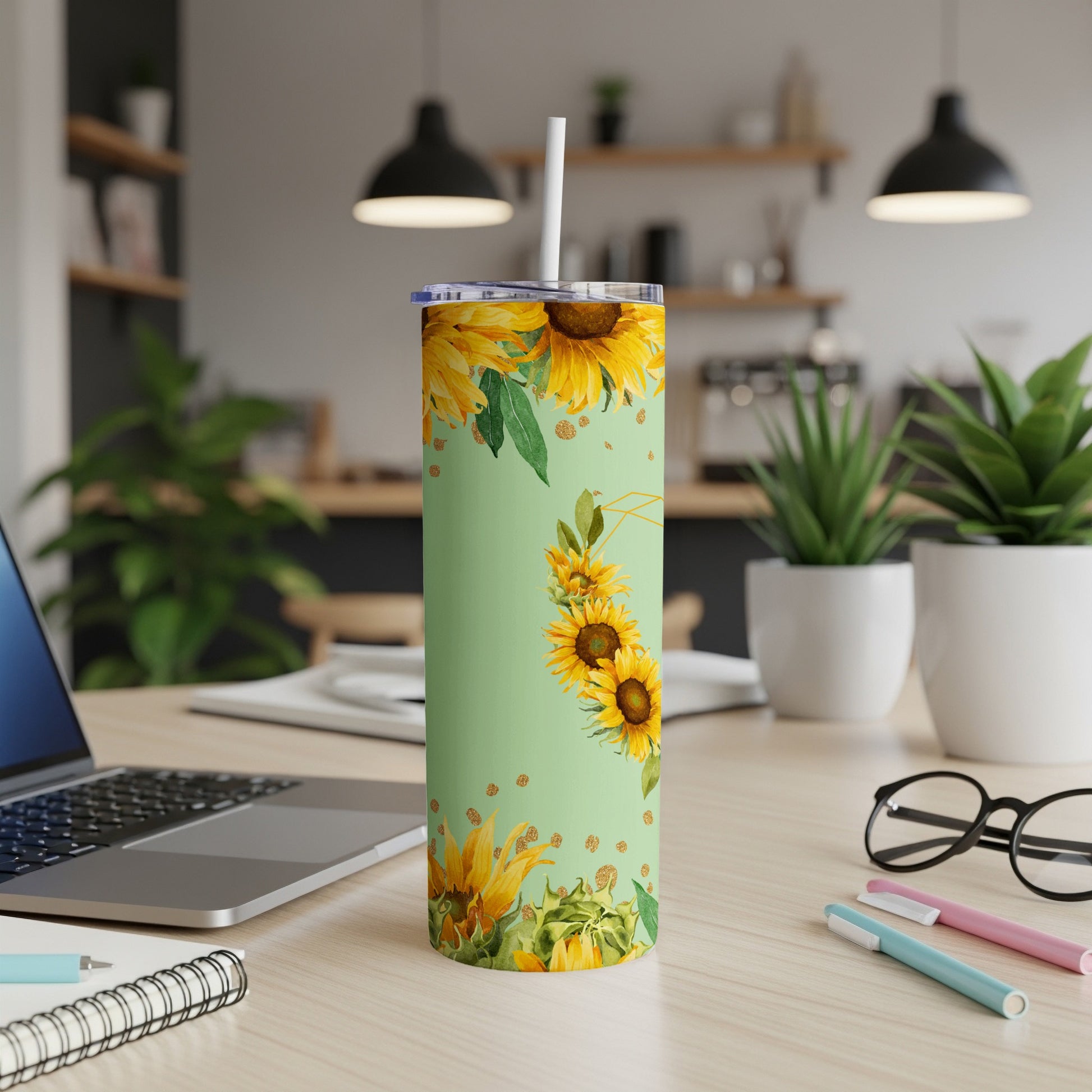 Green tumbler with sunflowers and leaves on a desk with a laptop.