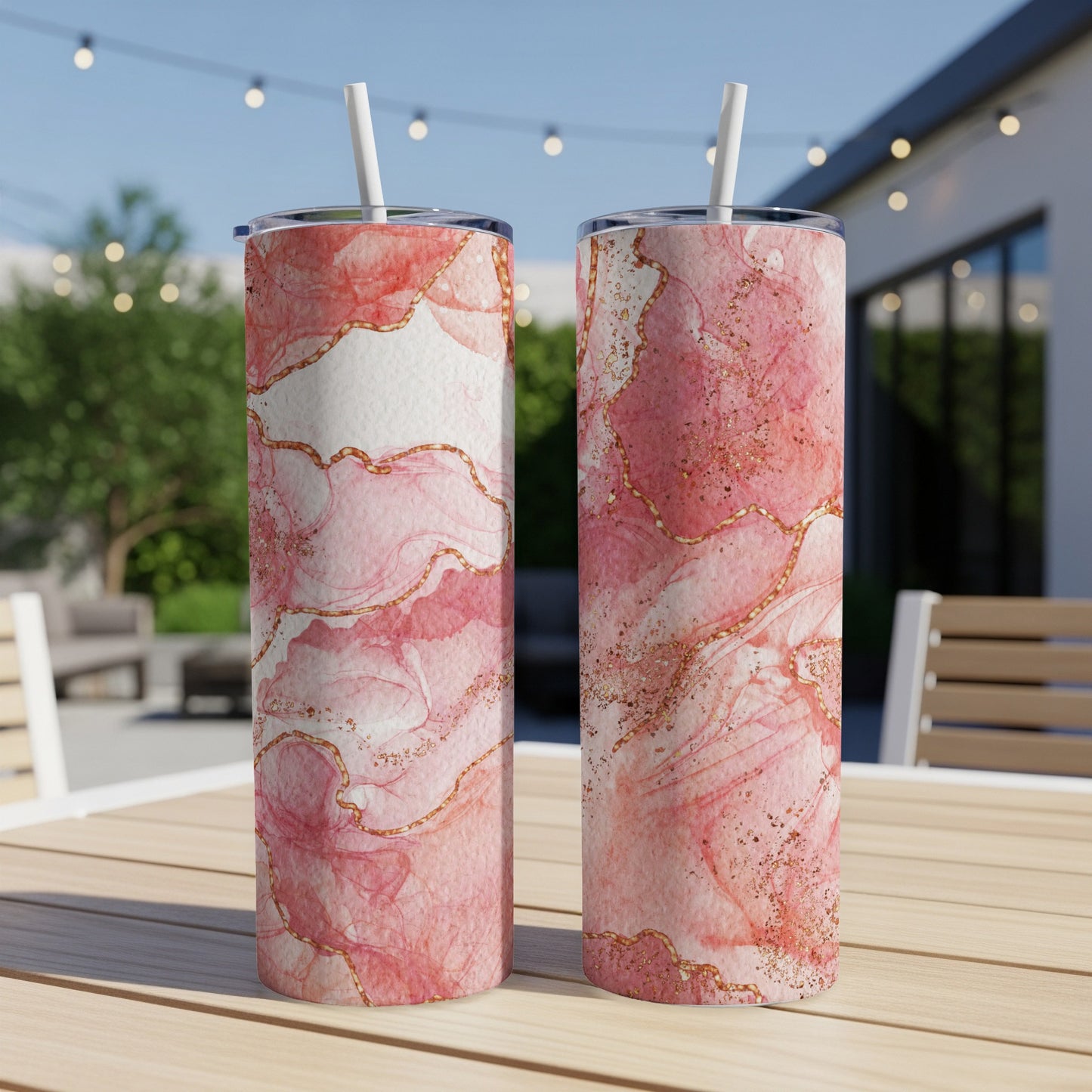 Two pink marble pattern tumblers with gold glitter and straws on a table.