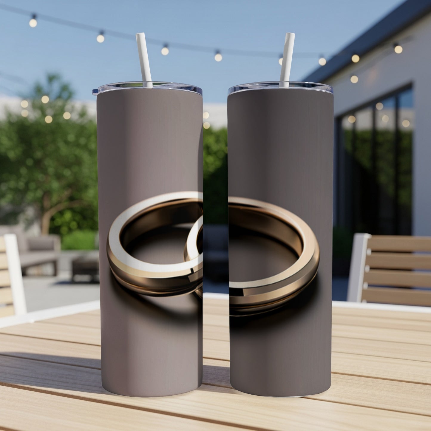 Two matching tumblers with a gold ring design sit on a wooden table outdoors.