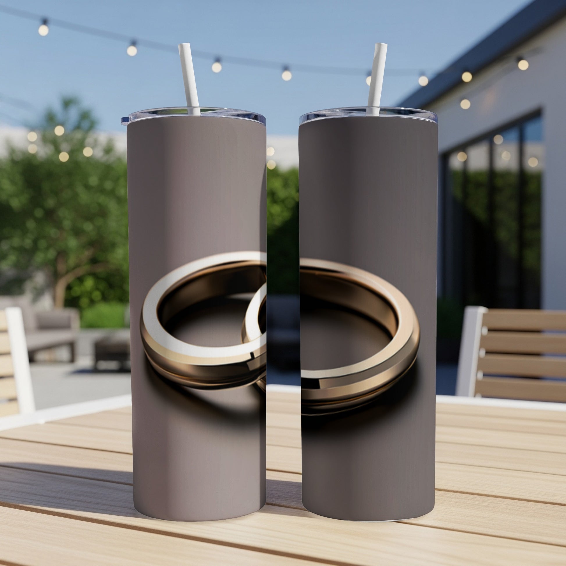 Two matching tumblers with a gold ring design sit on a wooden table outdoors.