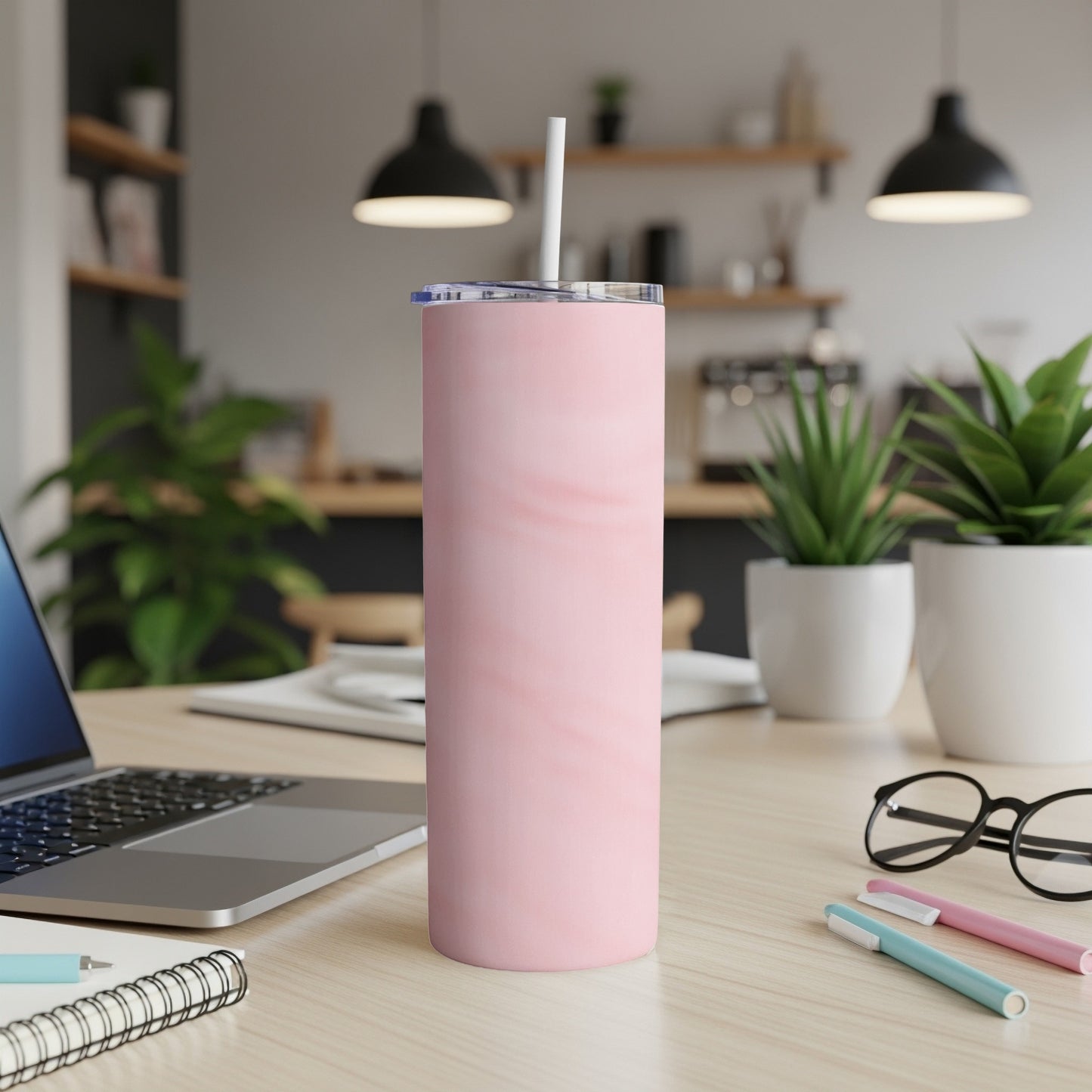 Pink marble tumbler with straw on a desk with laptop and pens.