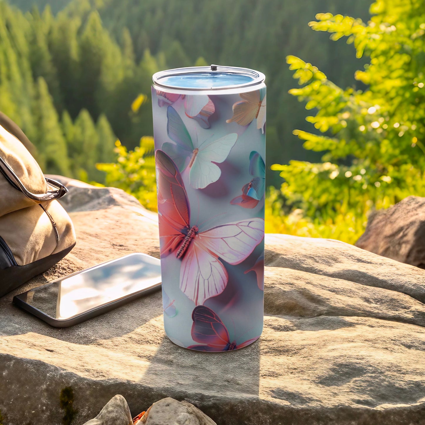 Tall tumbler with pastel butterfly design rests on rock beside backpack and phone.