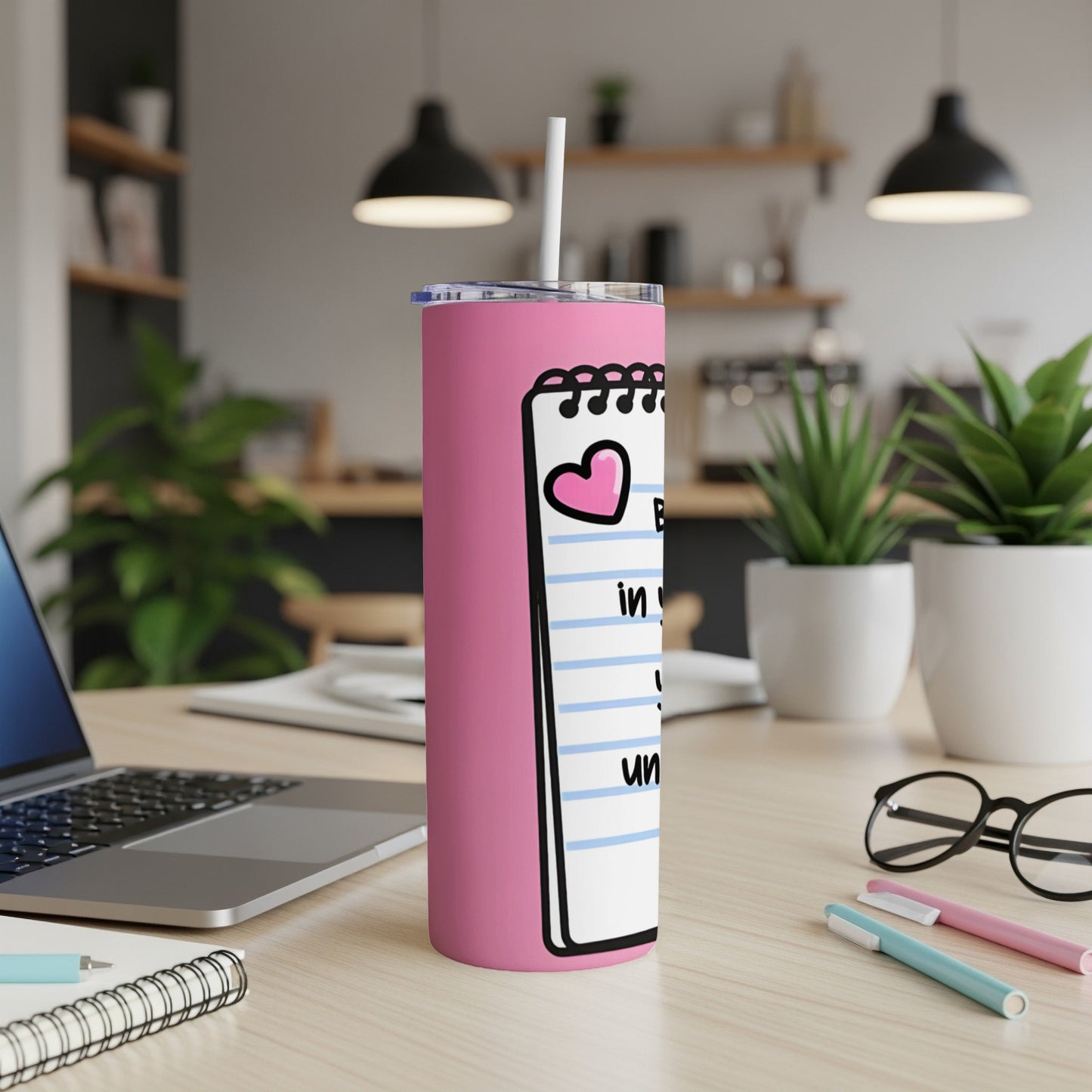 Pink tumbler with heart and "Be in love..." text on a desk.