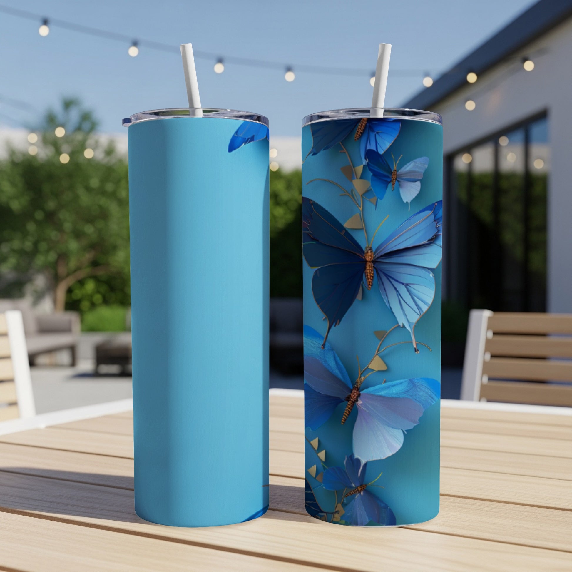 Two blue tumblers with butterfly designs on a table outdoors.