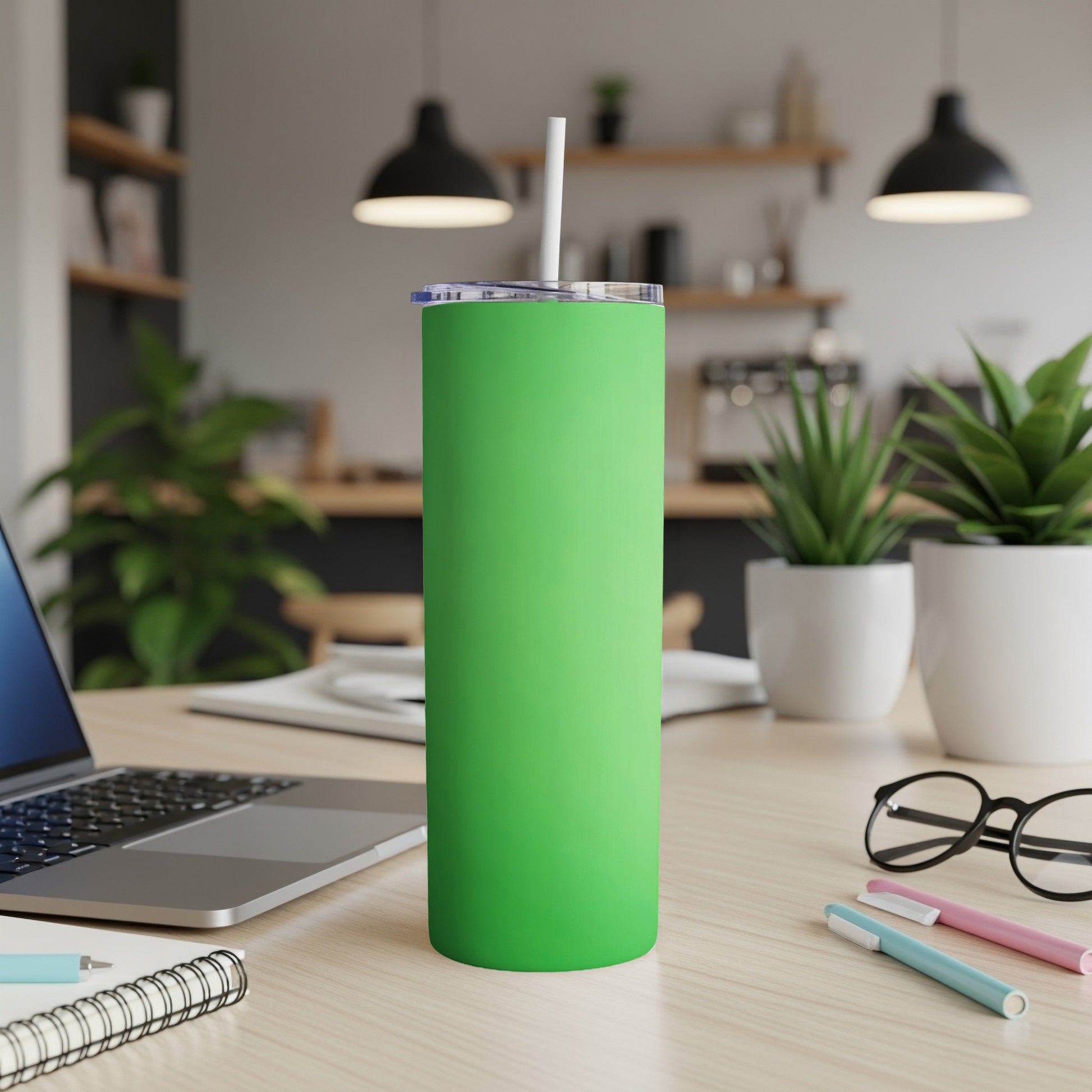 Green tumbler with straw on a desk, next to a laptop and pens.