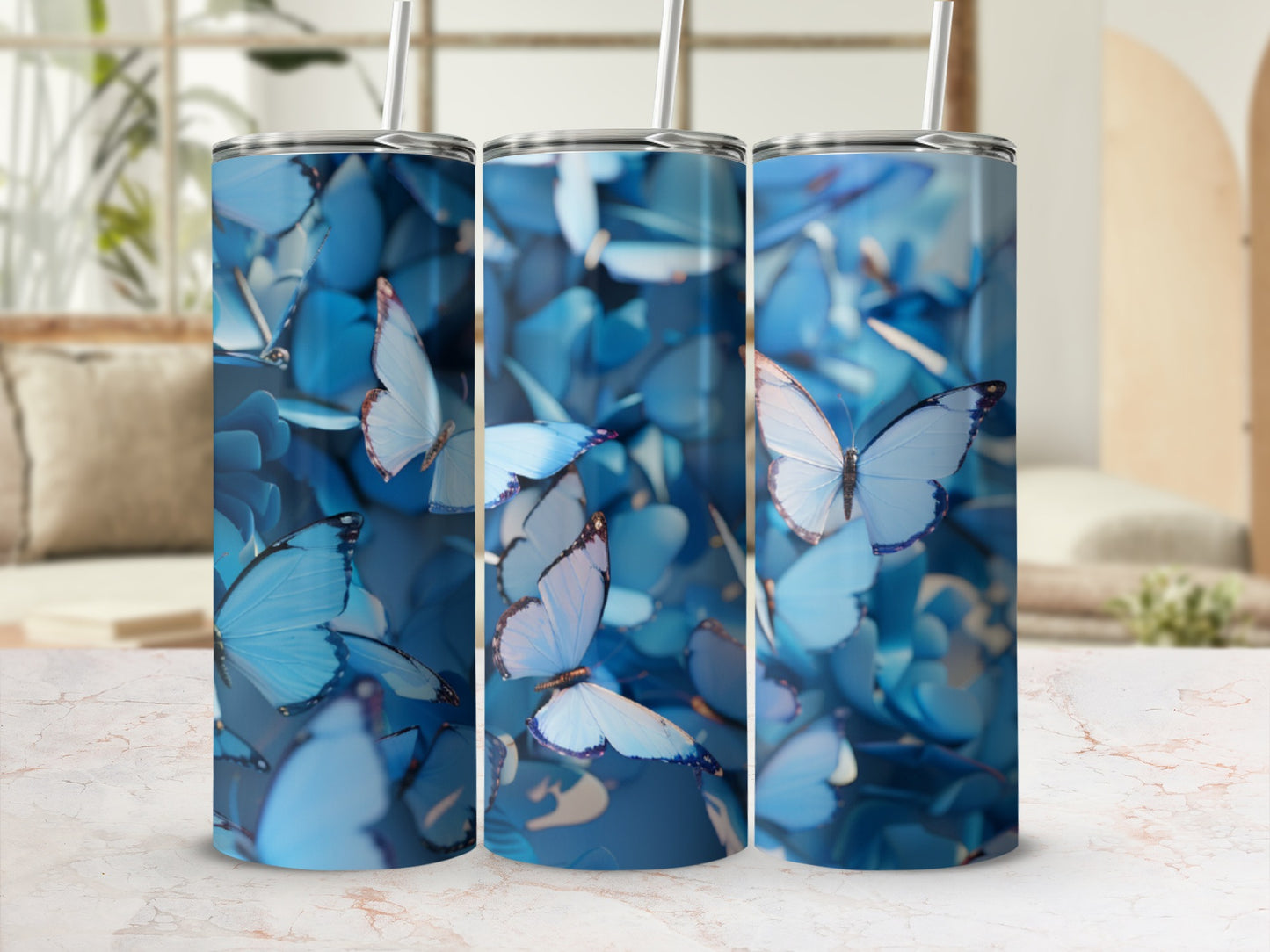 Three blue butterfly tumblers with straws on a marbled surface.