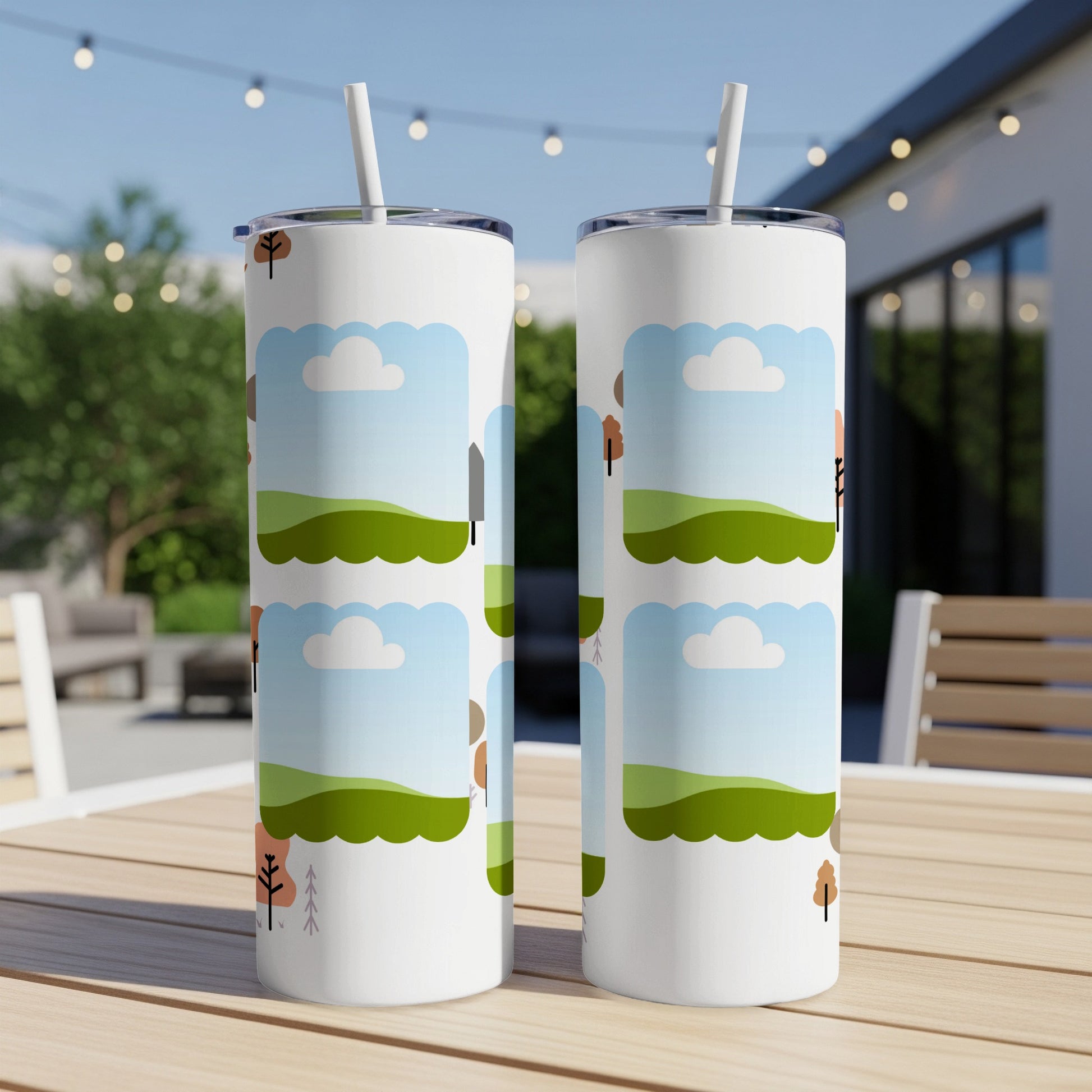 Two white tumblers with a cartoon landscape design, outdoors on a table.