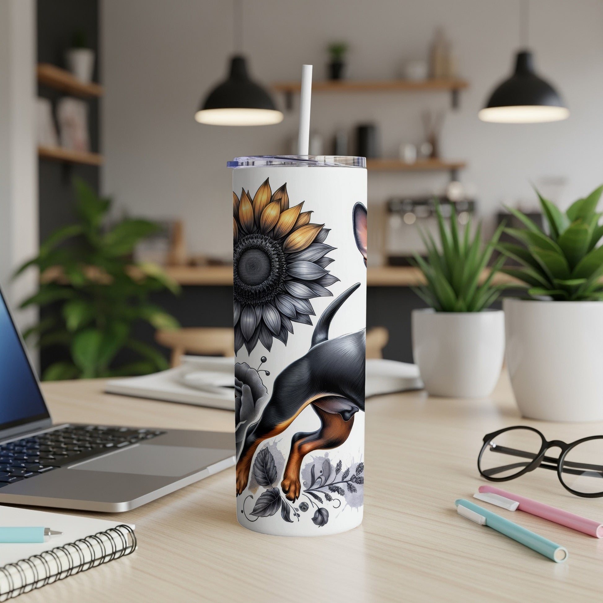 White tumbler with black dog and sunflower illustration on a desk.