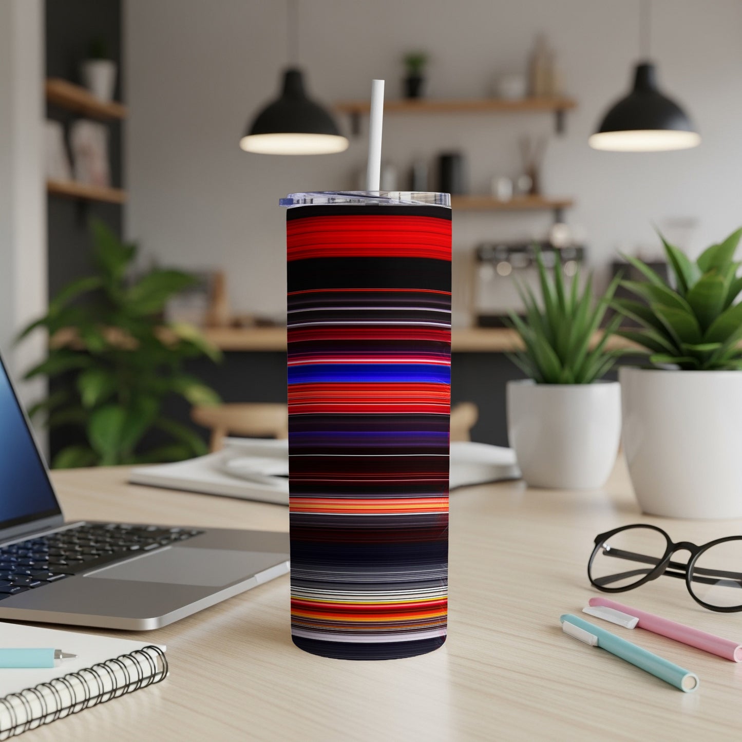 Striped tumbler with straw on a desk with a laptop and plants.