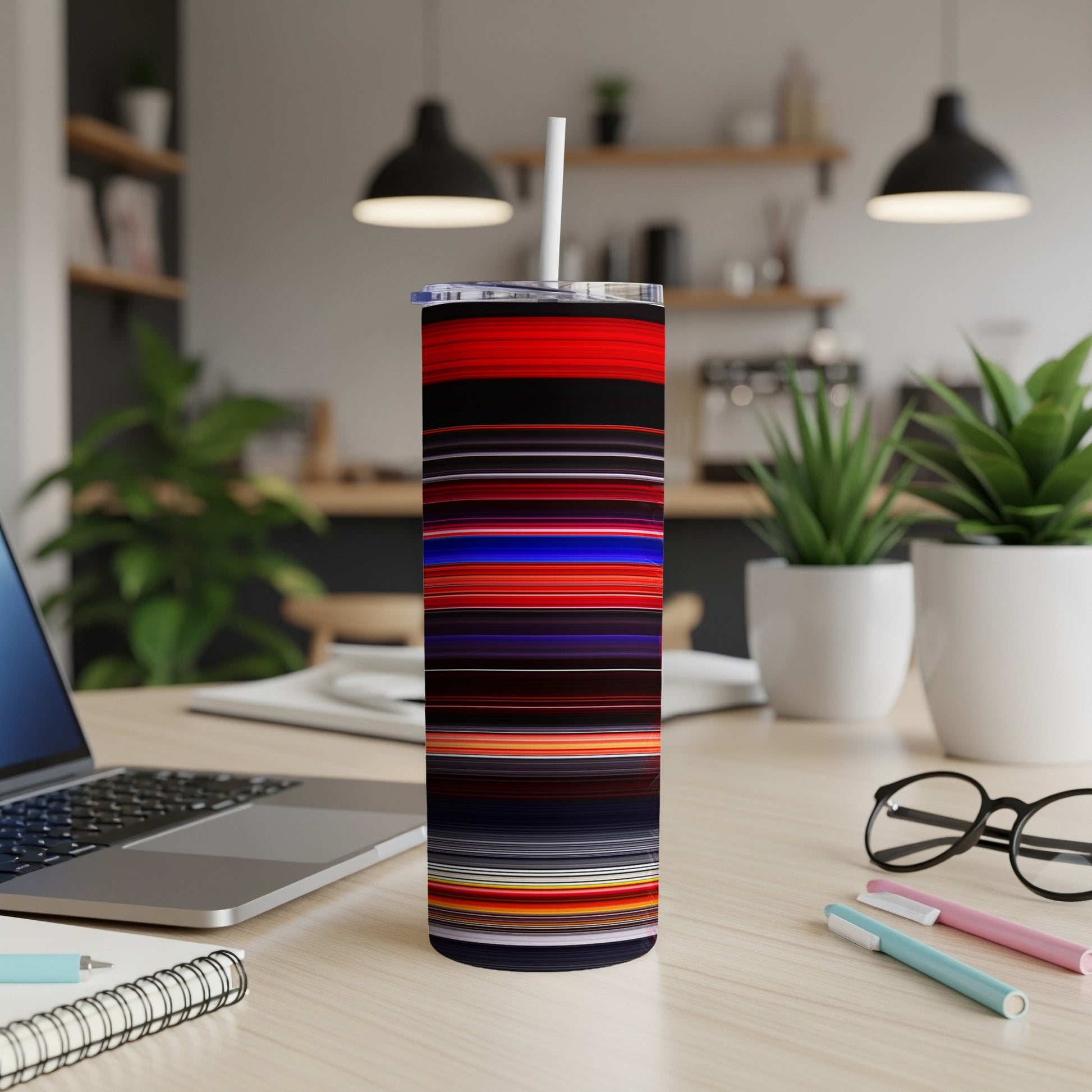 Striped tumbler with straw on a desk with a laptop and plants.