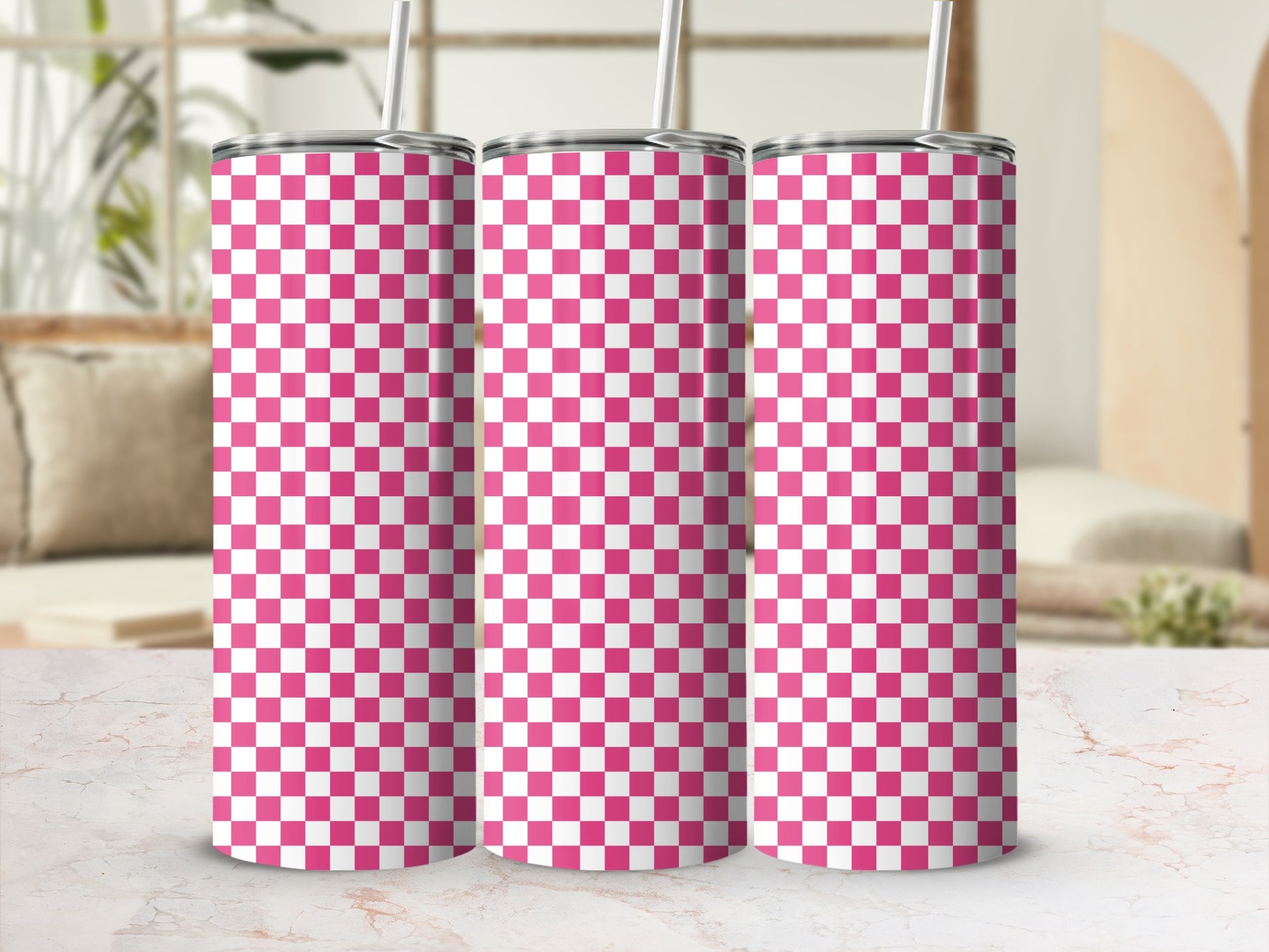 Three pink and white checkered tumblers with straws stand on a marble surface.