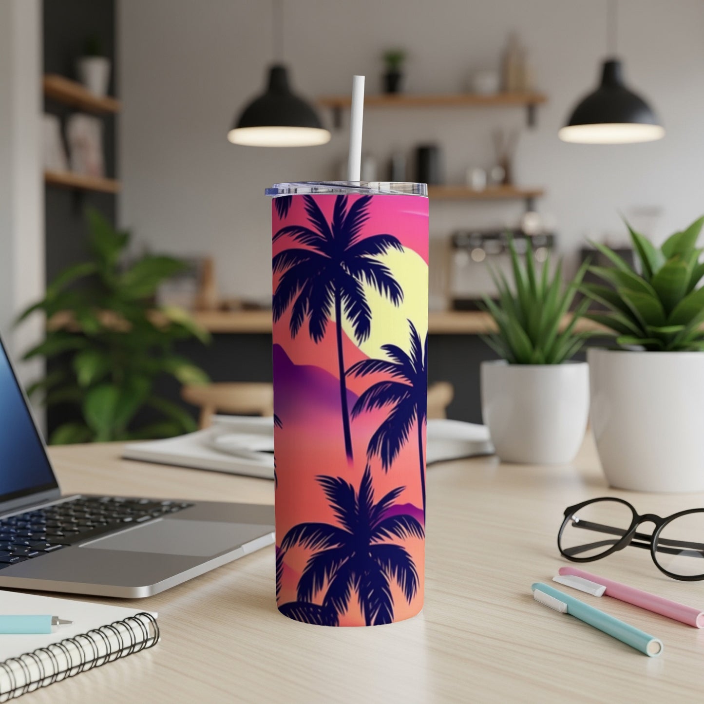 Tall tumbler with sunset palm trees design, white straw, on desk.