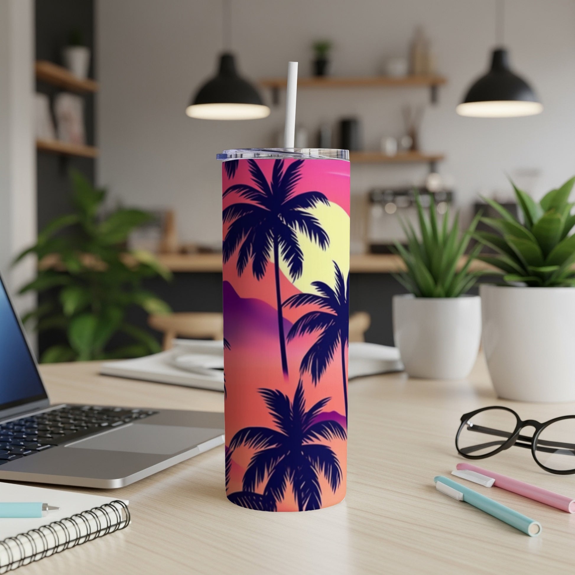 Tall tumbler with sunset palm trees design, white straw, on desk.
