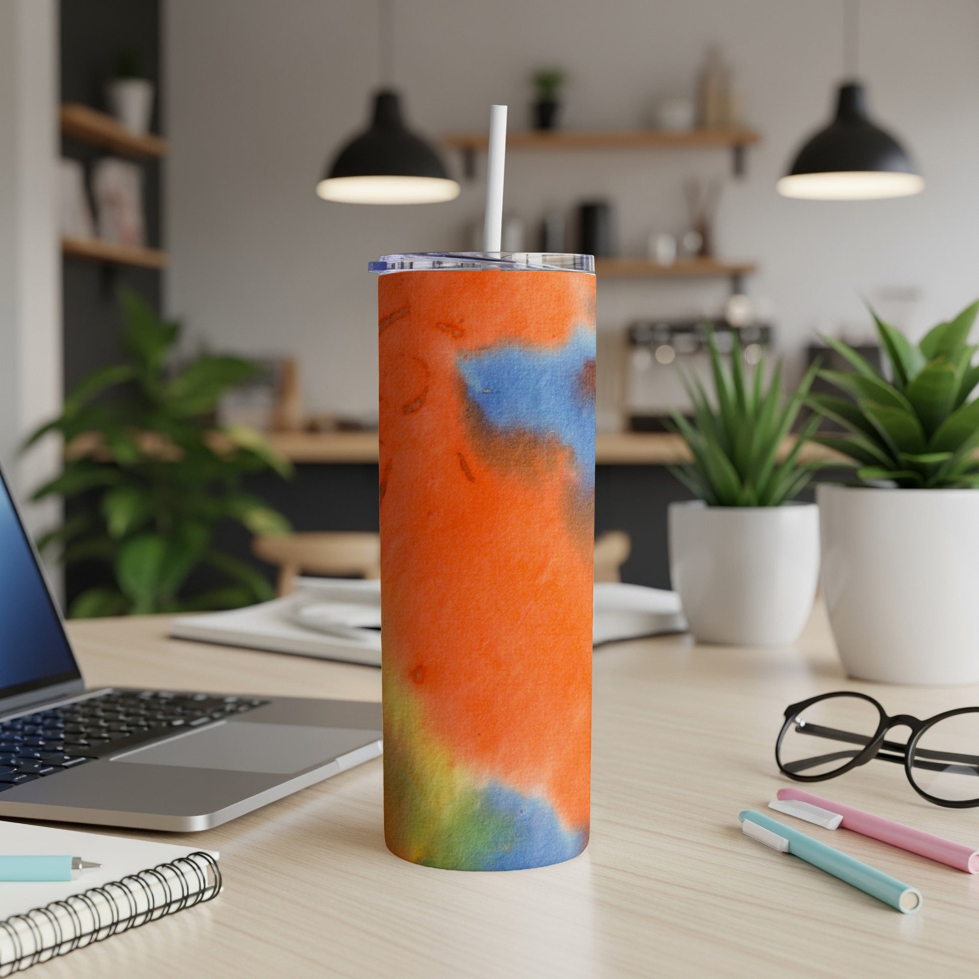 Orange, blue, and yellow tie-dye tumbler with straw on desk.