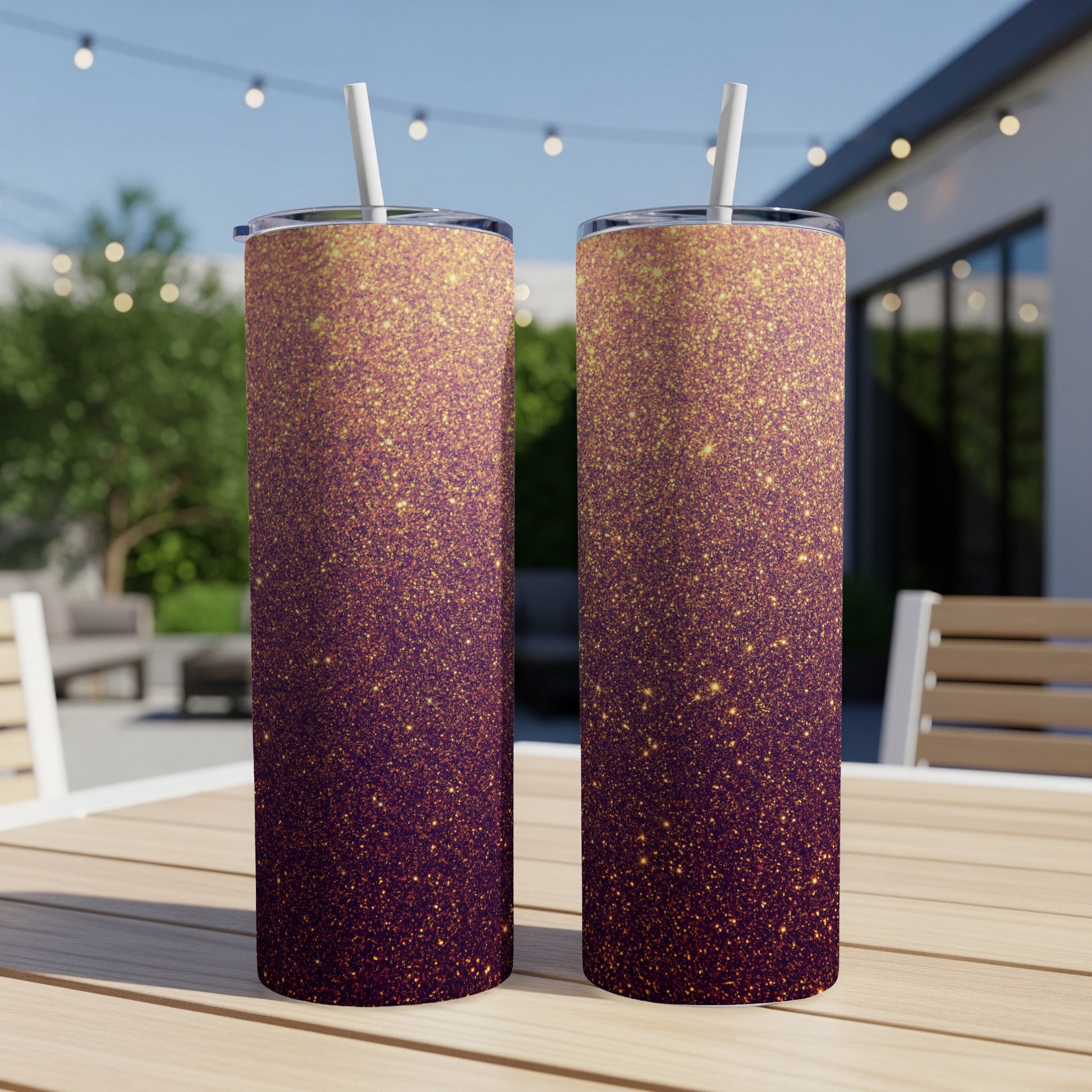 Two tall tumblers with a purple to gold glitter gradient design on a table.