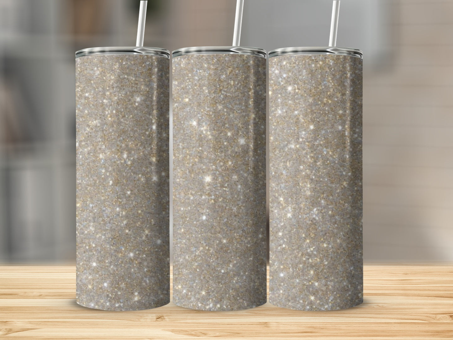 Three tall, glitter-covered tumblers with white straws on a wooden surface.