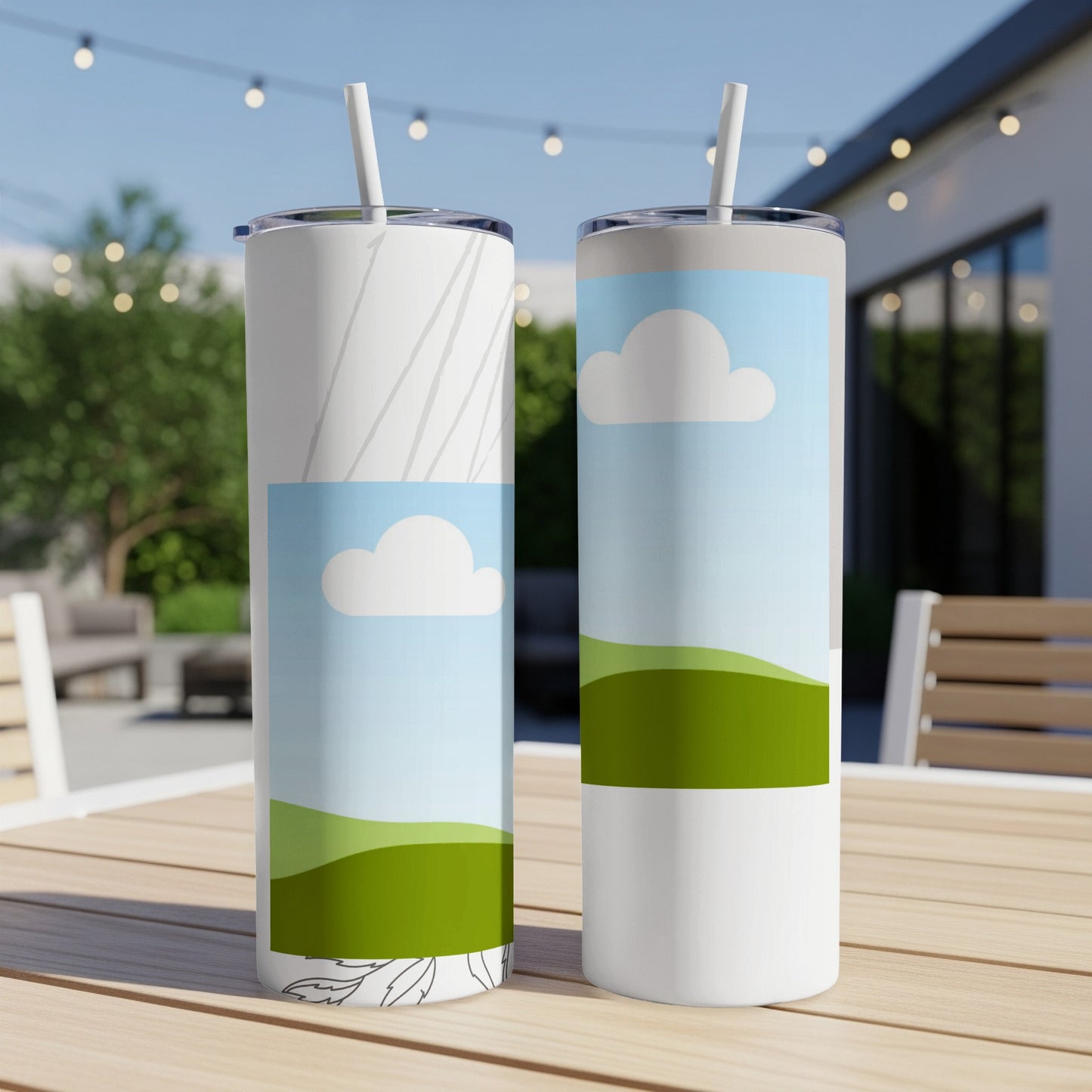 Two tumblers with landscape and cloud designs sit on a wooden table outdoors.