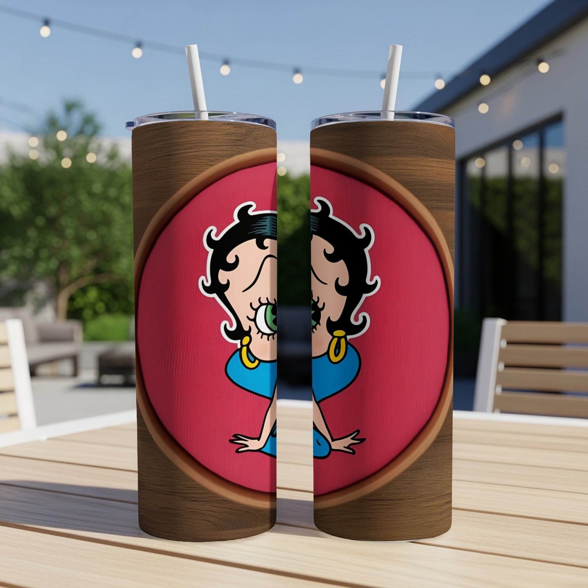 Two Betty Boop tumblers with straw on a wooden table outdoors.
