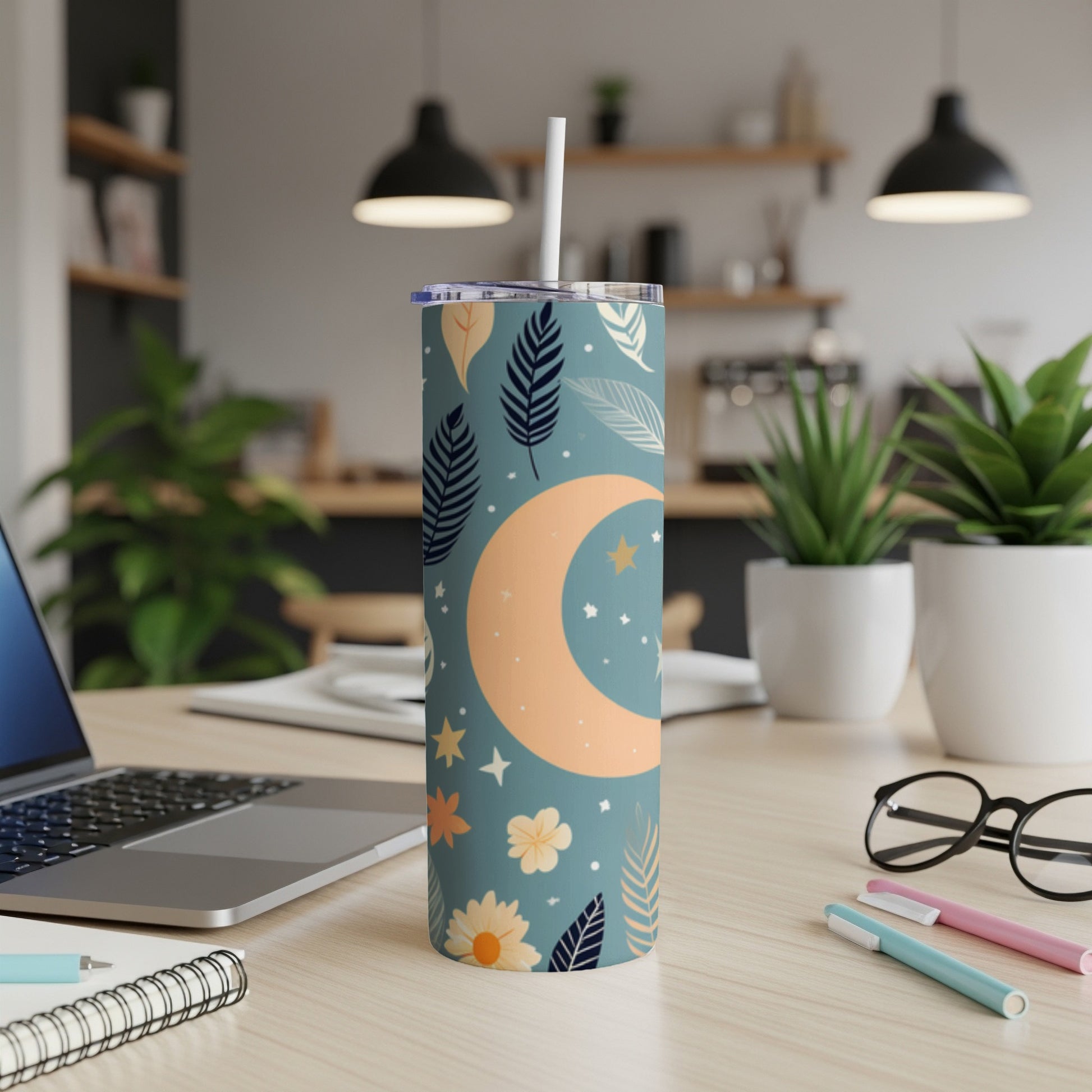 Tall teal tumbler with moon and star pattern, on a desk.