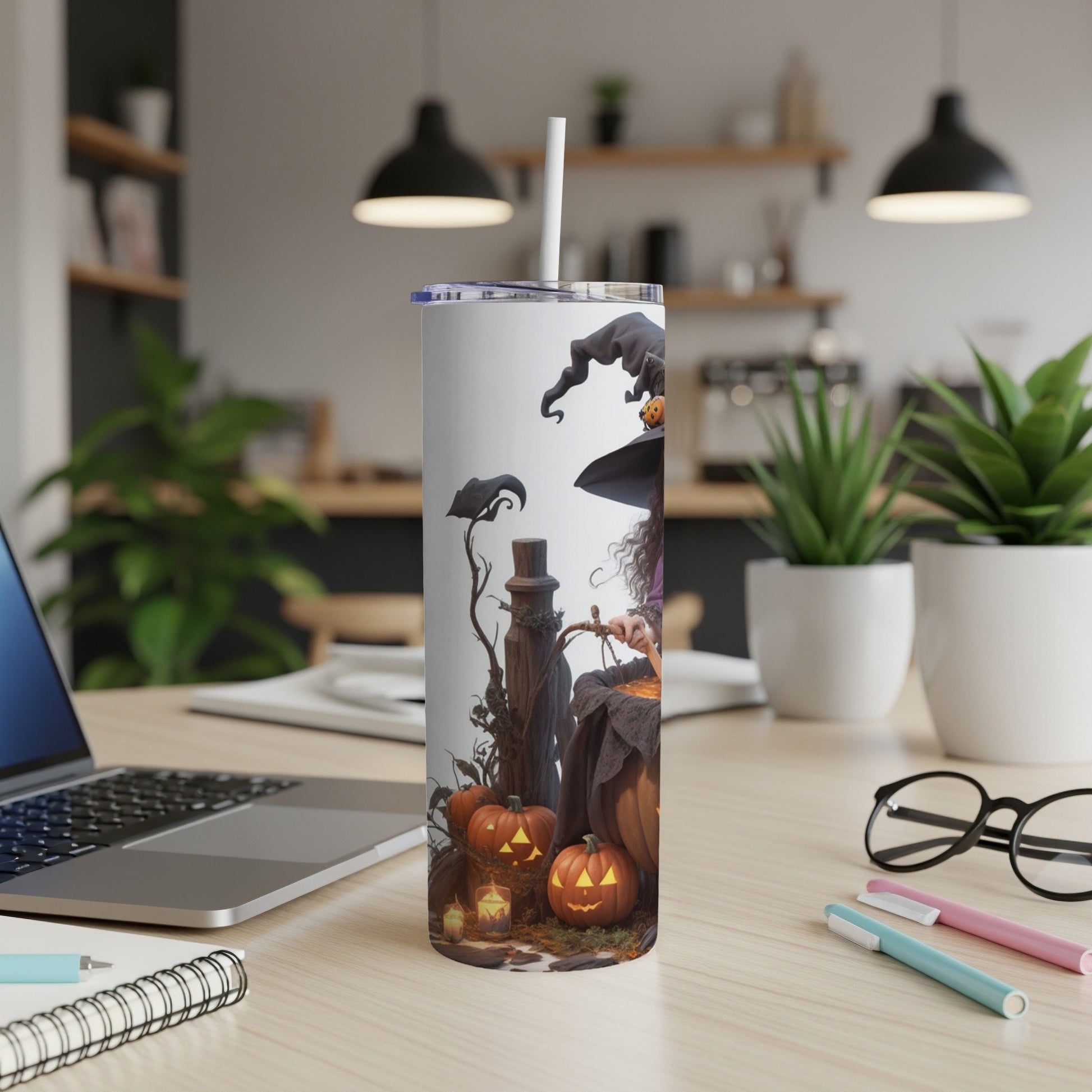 Tumbler with witch, pumpkins, and candles with a straw in a workspace.