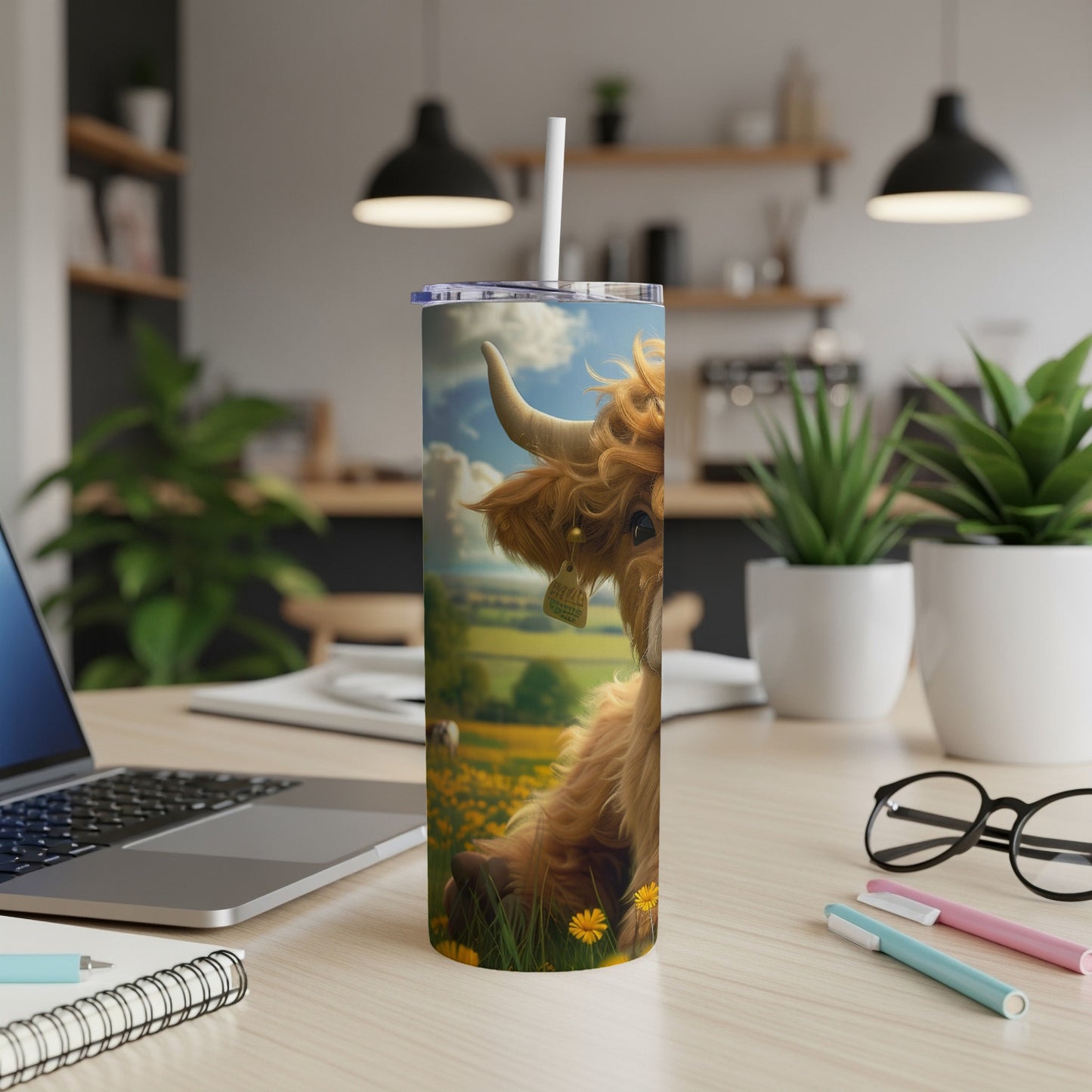 Highland cow illustration on a skinny tumbler with a straw, on a desk.