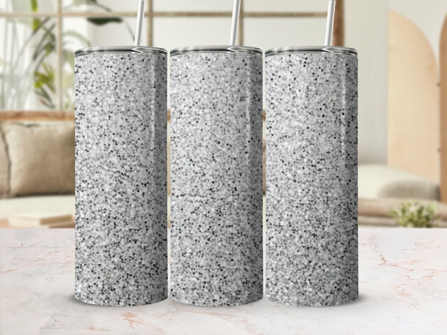 Three silver glitter tumblers with straws on a marble surface.