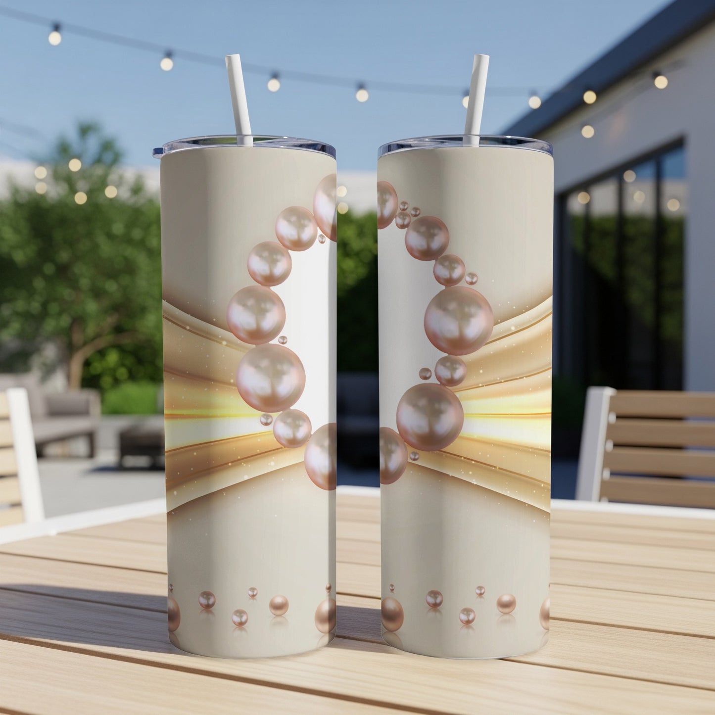 Two tumblers with a pearl and gold wave design displayed on a wooden table outdoors.