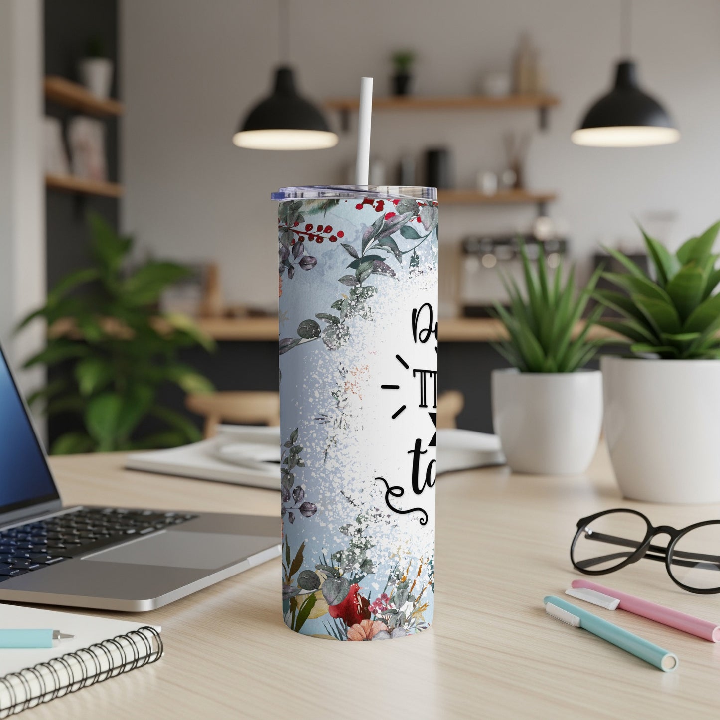 Floral patterned tumbler with white lid and straw on a desk.