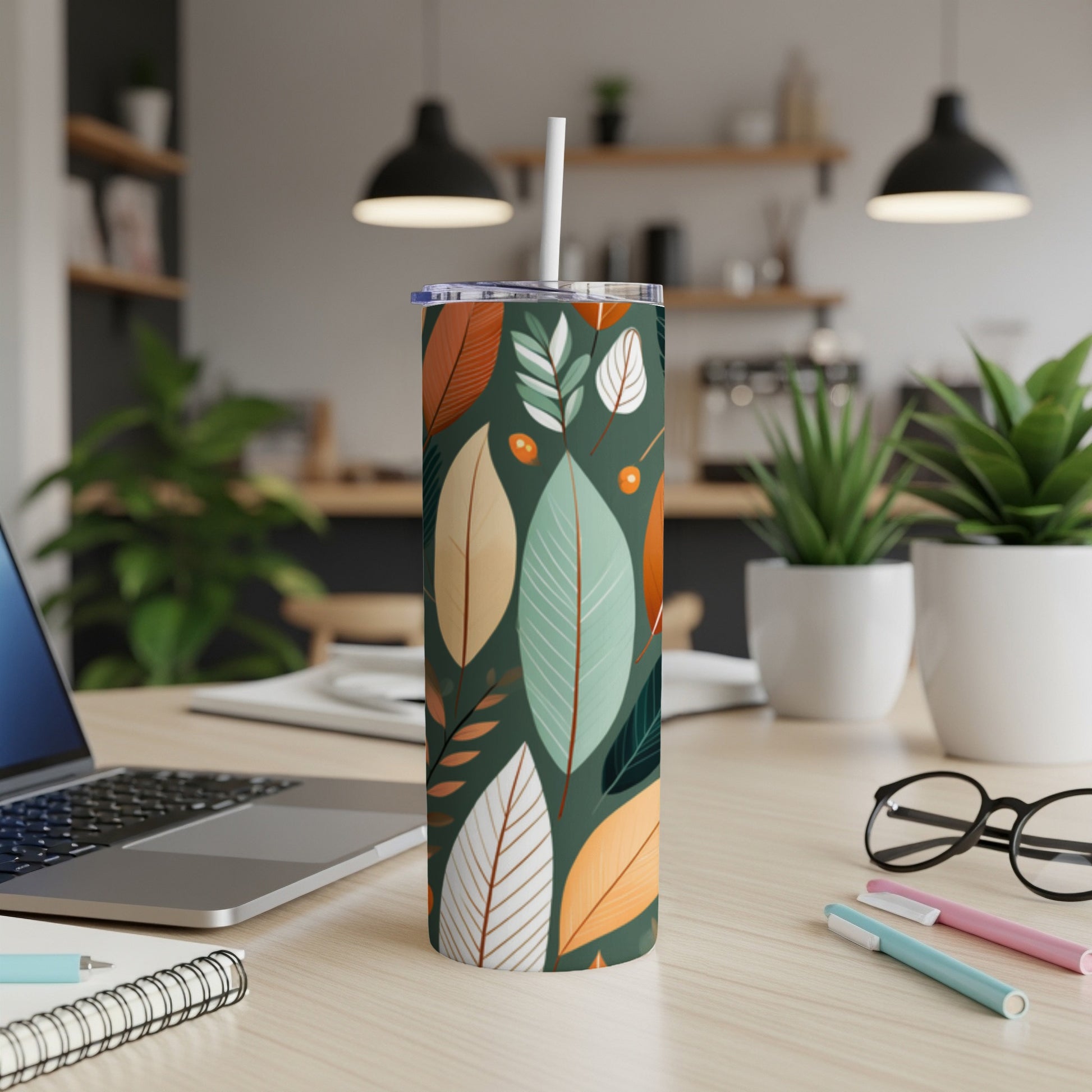 Tall tumbler with green, teal, and orange leaf pattern on a desk.