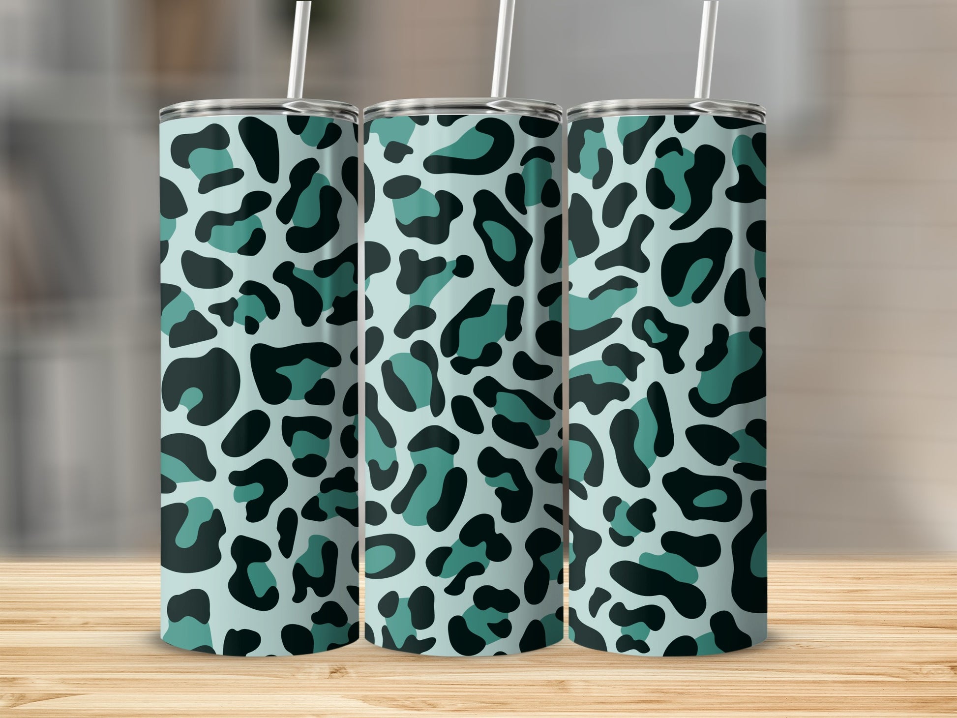 Three tumblers with teal and black leopard print designs stand on a wooden surface.