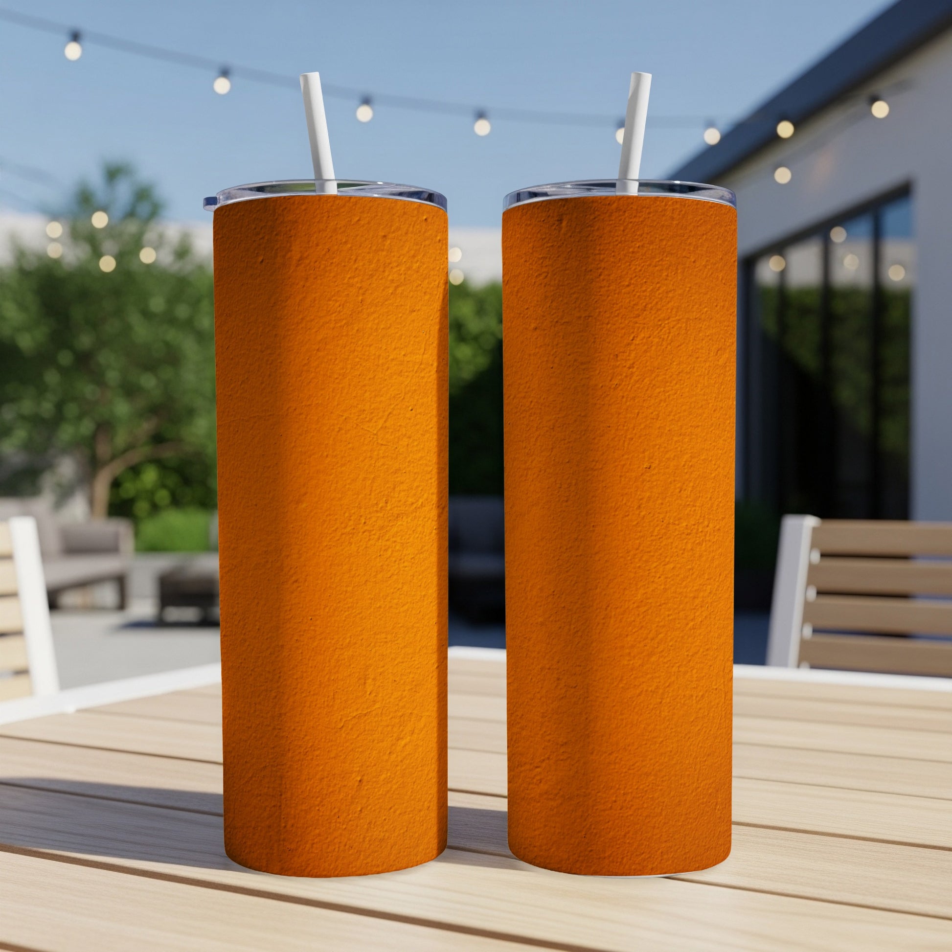 Two textured orange tumblers with white straws on a wooden table.