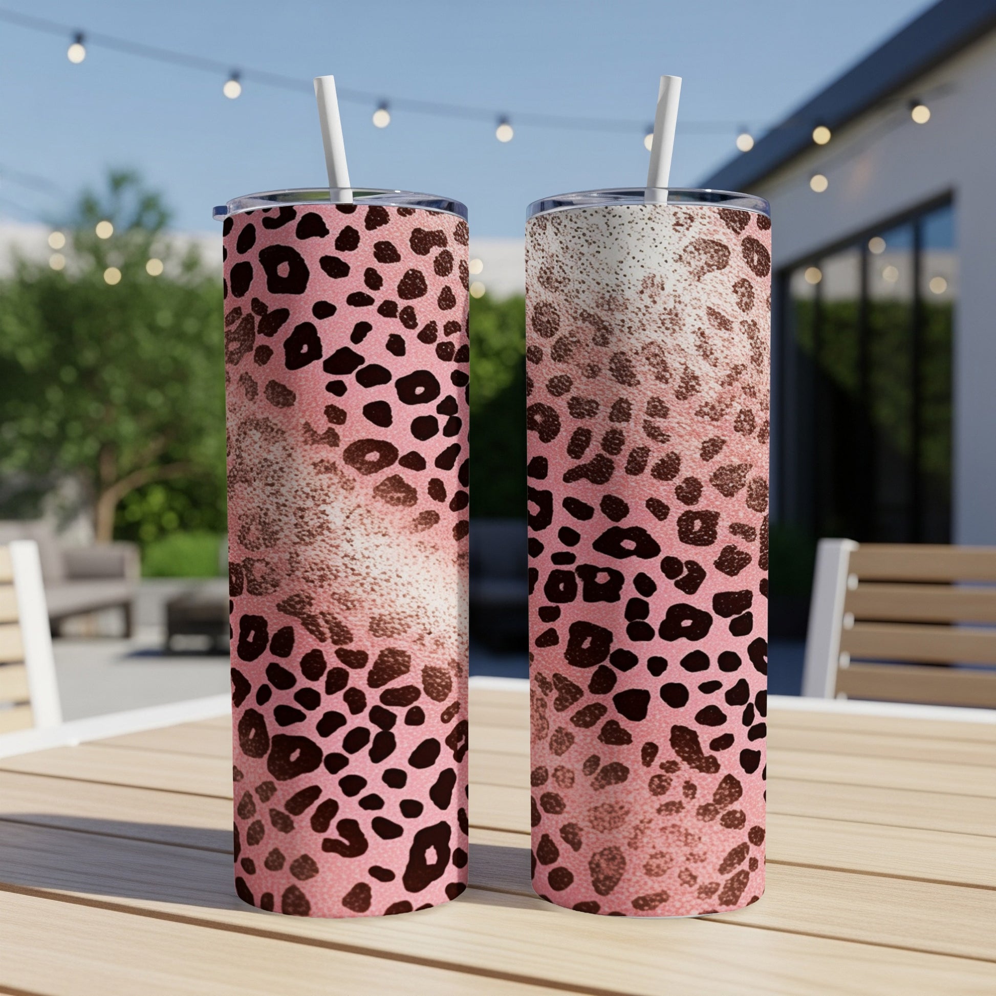 Two pink leopard print tumblers with straws on a table.