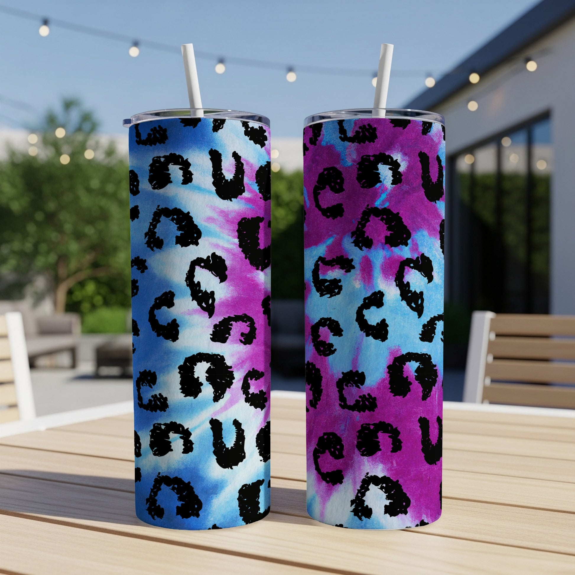 Two tumblers with tie-dye and leopard print designs stand on a wooden table.