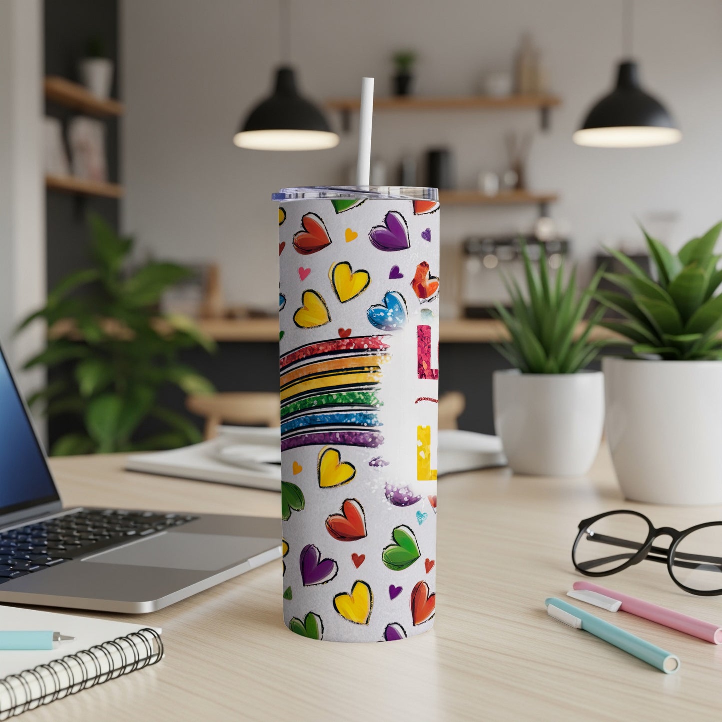 Rainbow hearts pattern tumbler with straw and laptop on desk.
