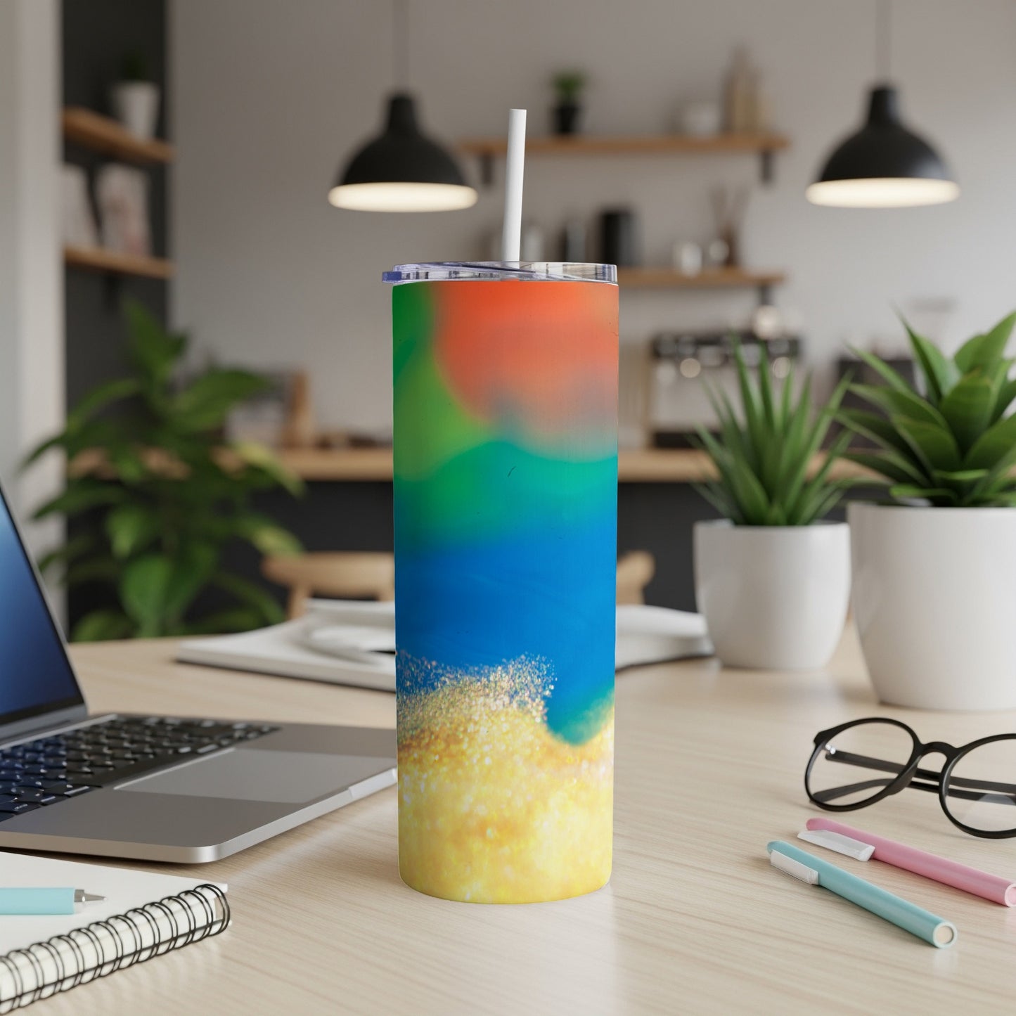 Colorful abstract tumbler with straw on a desk next to a laptop.