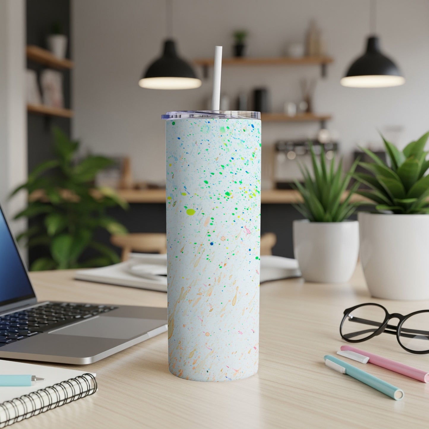 White skinny tumbler with colorful paint splatters and a straw.