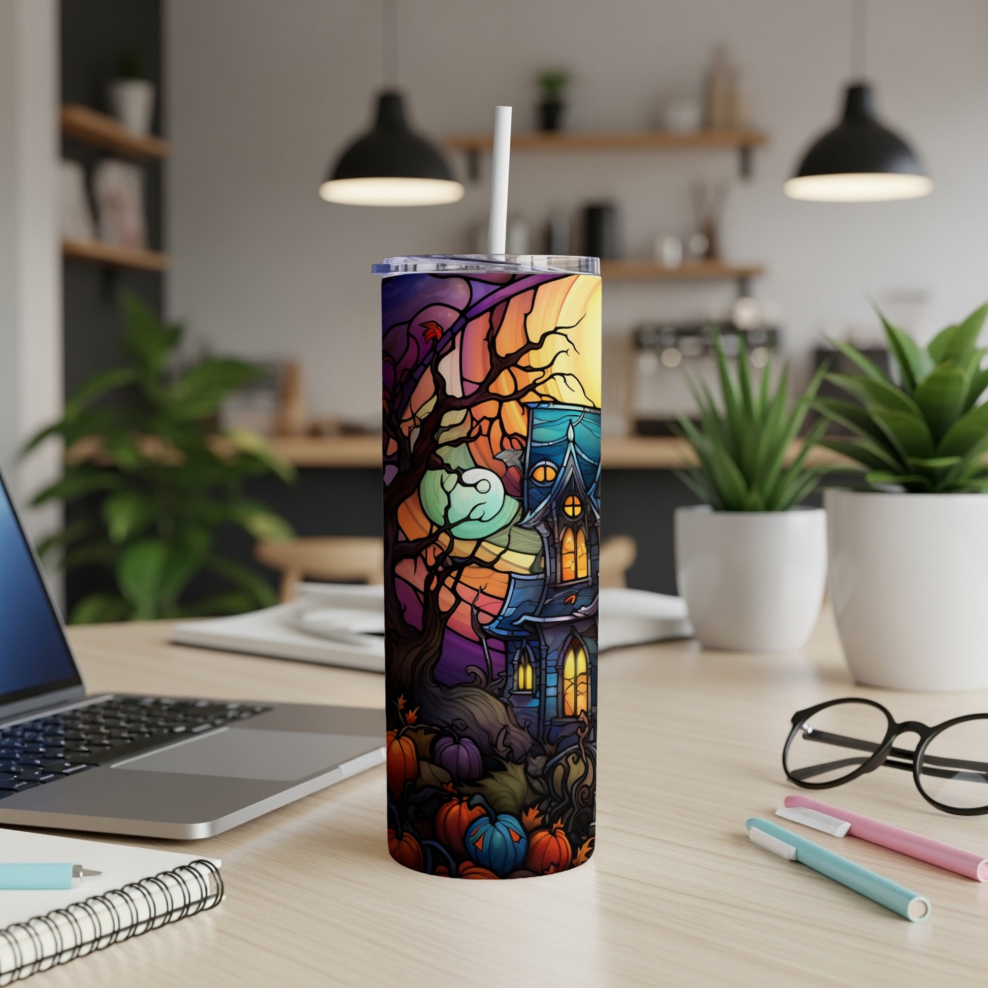 Halloween tumbler with haunted house and pumpkins, on desk.