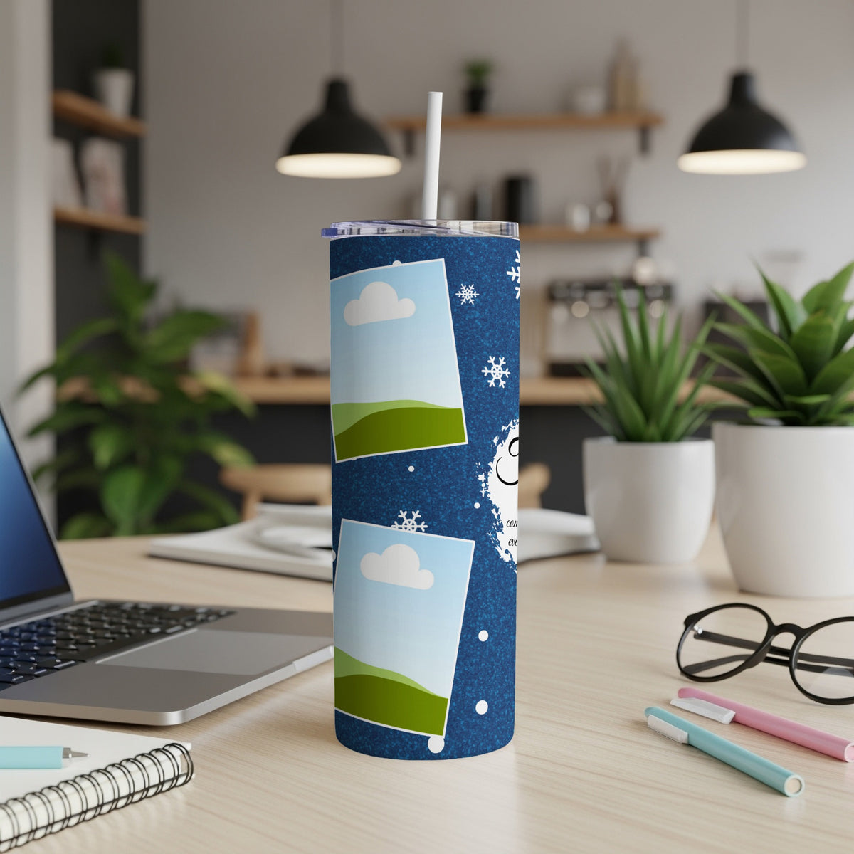 Blue tumbler with snow globes and snowflakes on a desk with a laptop.