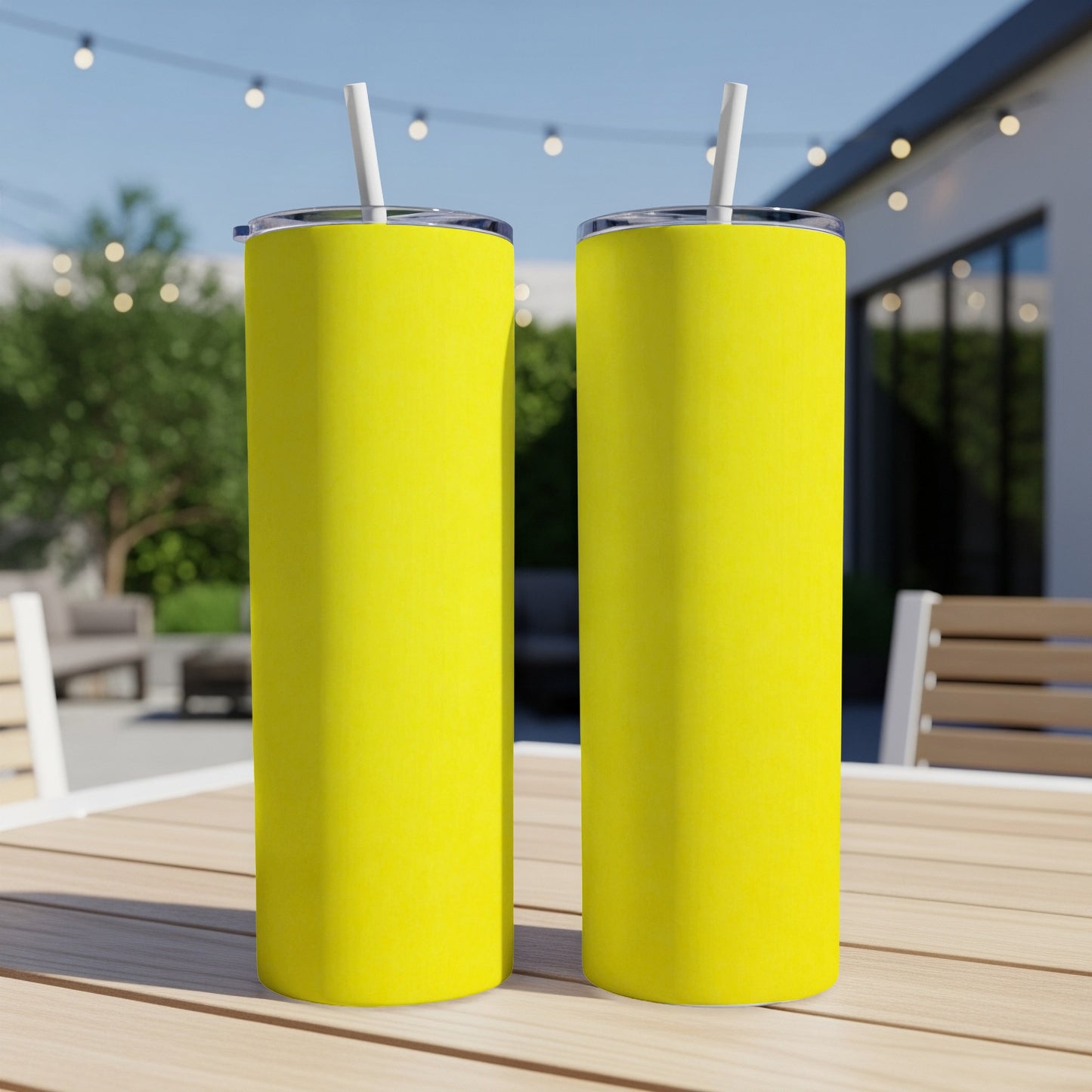 Two yellow tumblers with straws on a wooden table outdoors.