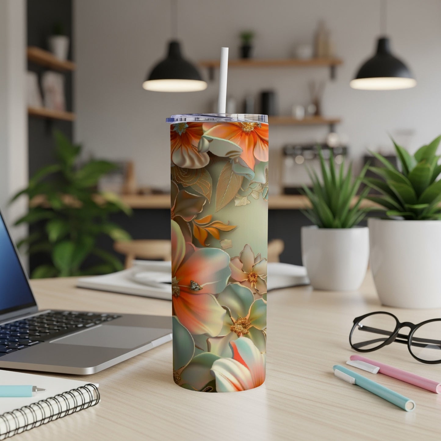 Floral tumbler with straw on desk next to laptop and pens.