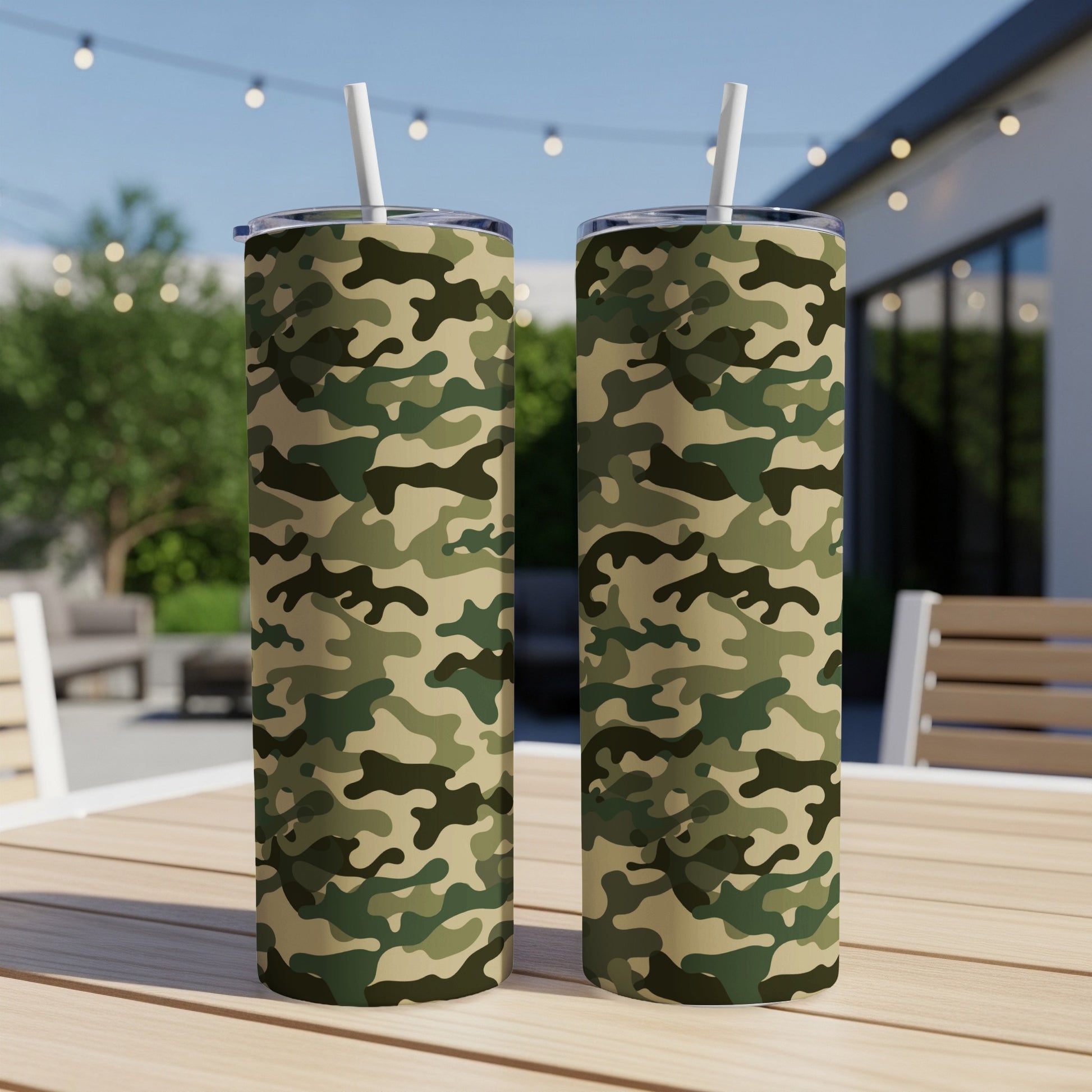 Two camouflage pattern tumblers with white straws on a wooden table outdoors.
